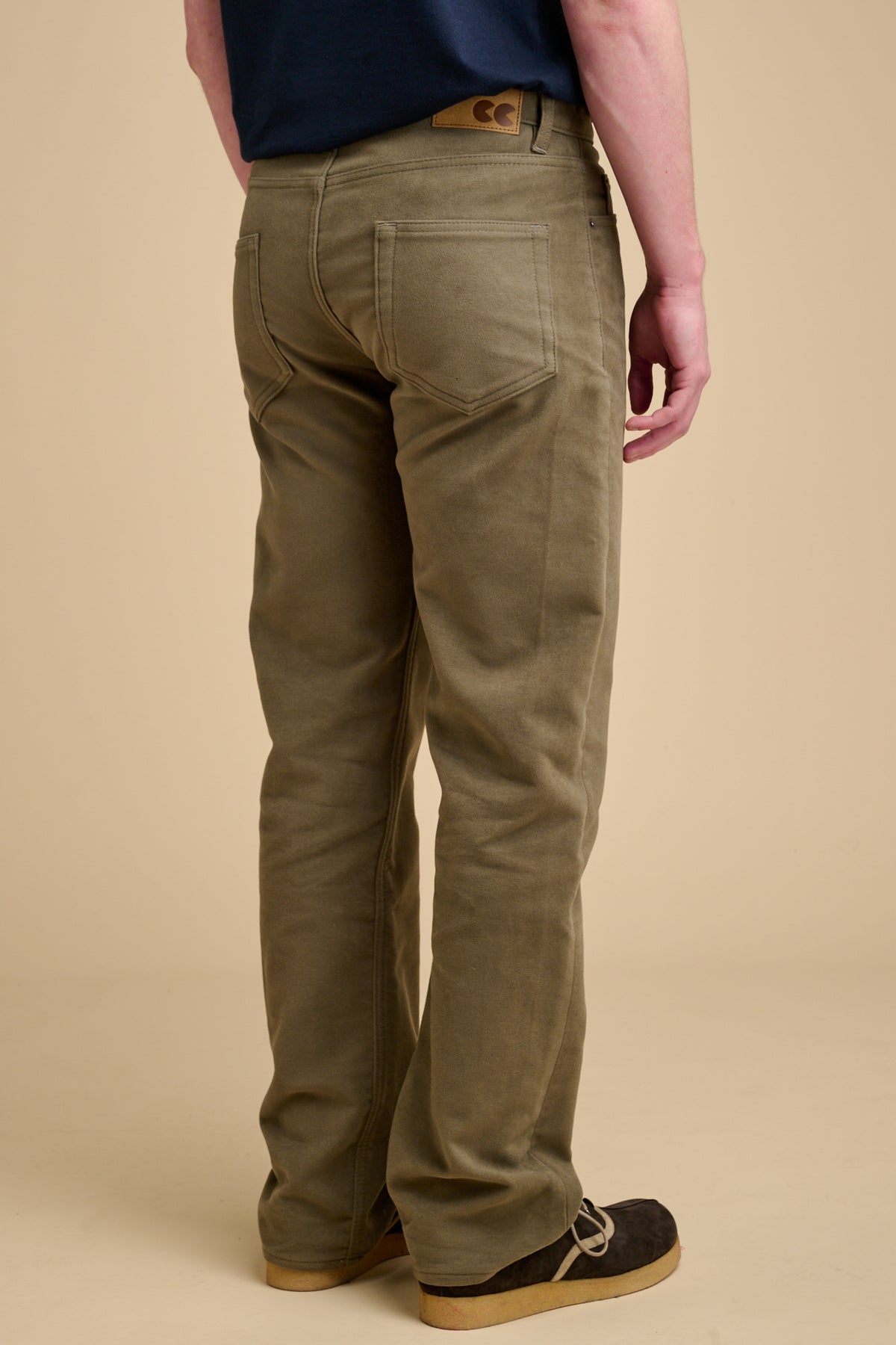 The back of male wearing olive moleskin jeans on beige background.