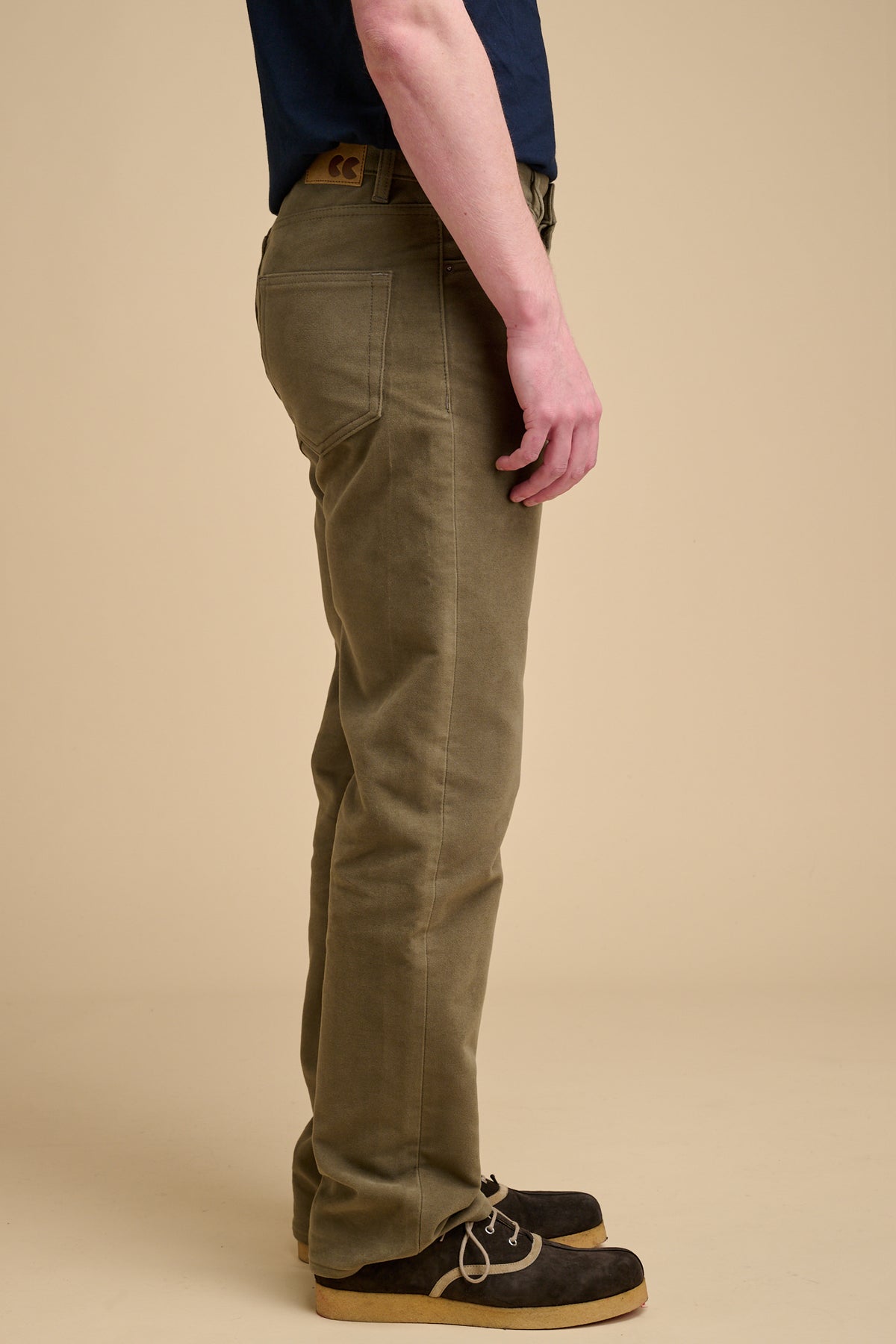 Male wearing olive moleskin jeans on beige background.