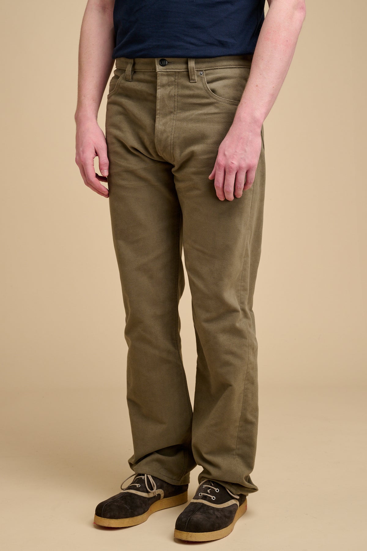 Male wearing olive moleskin jeans on beige background.