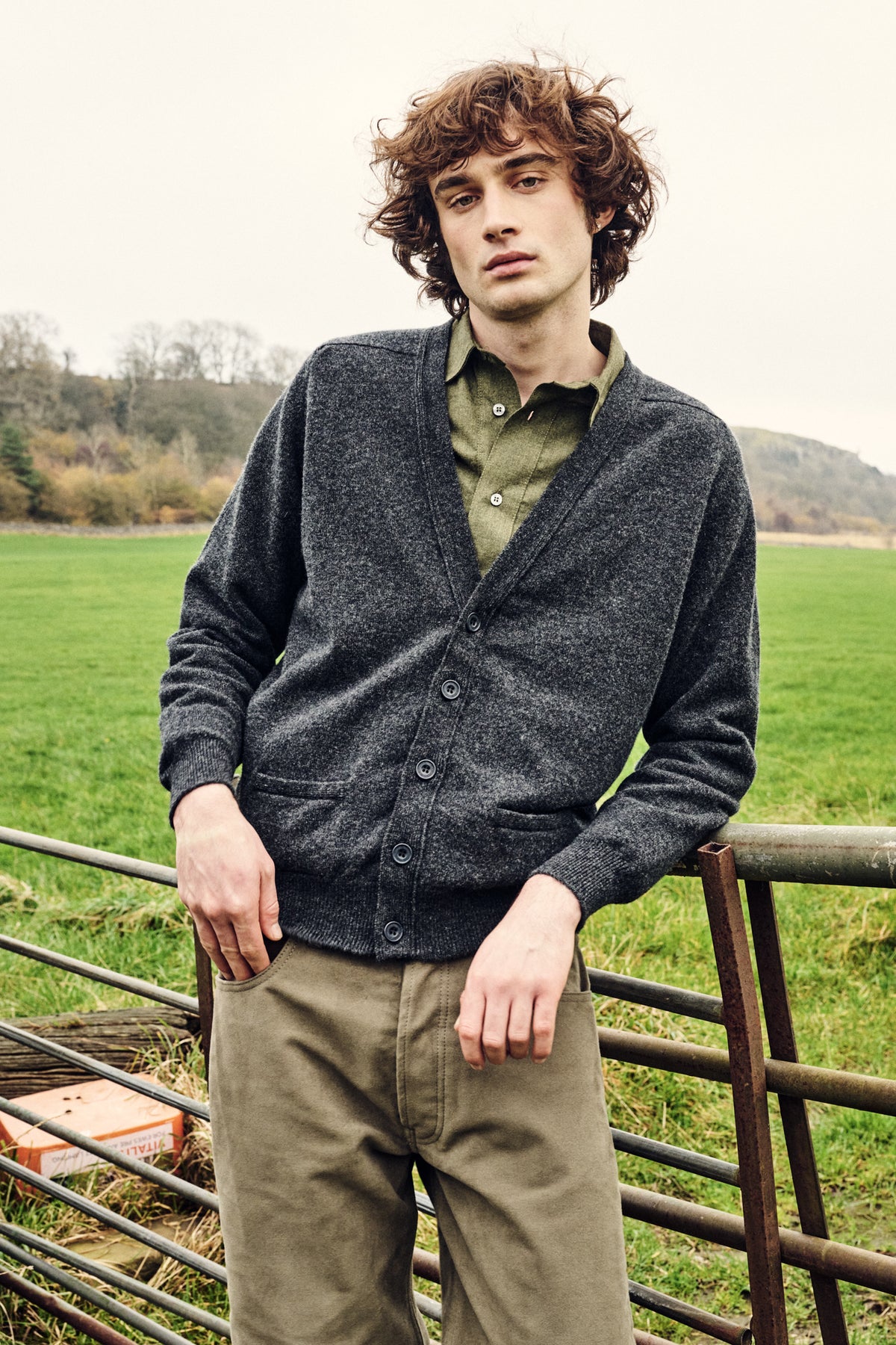 Man wearing a dark grey cardigan over a green shirt with green trousers in a field