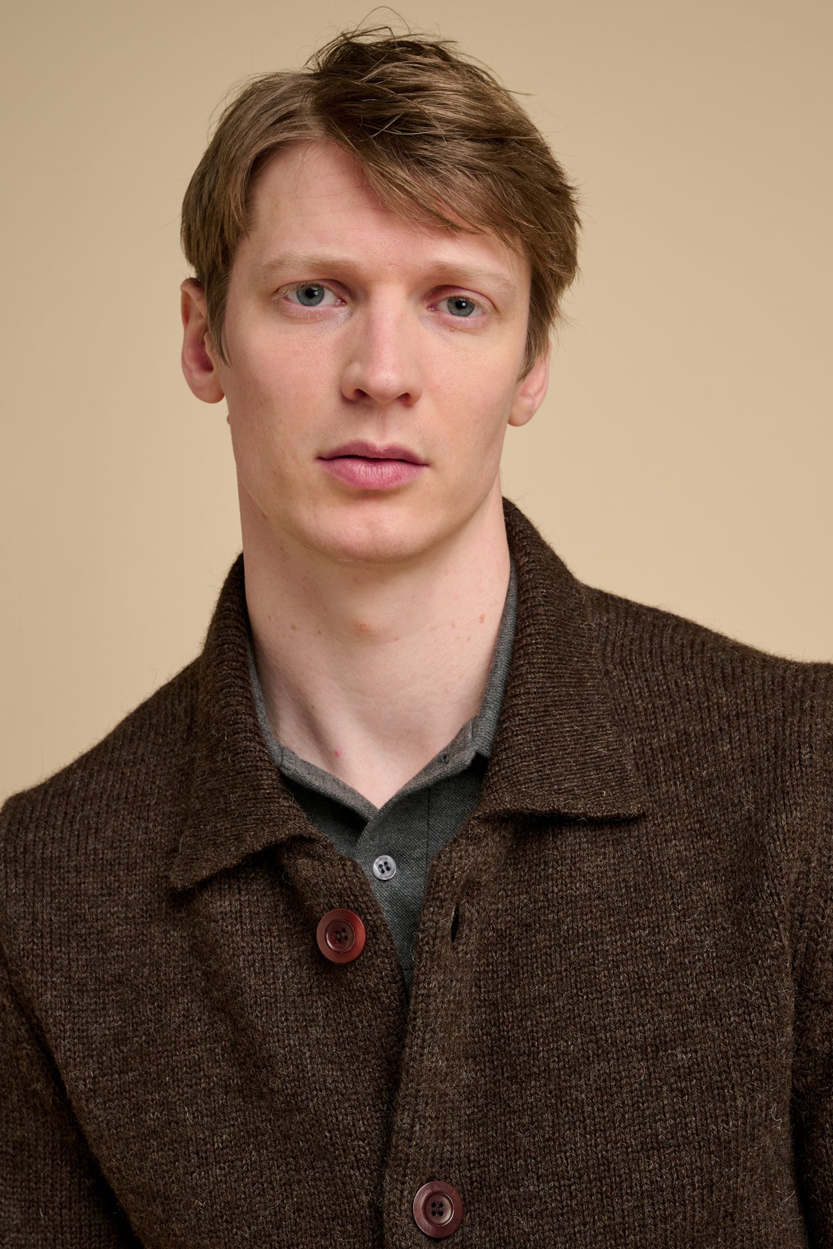 Man wearing a brown knitted cardigan against a beige background