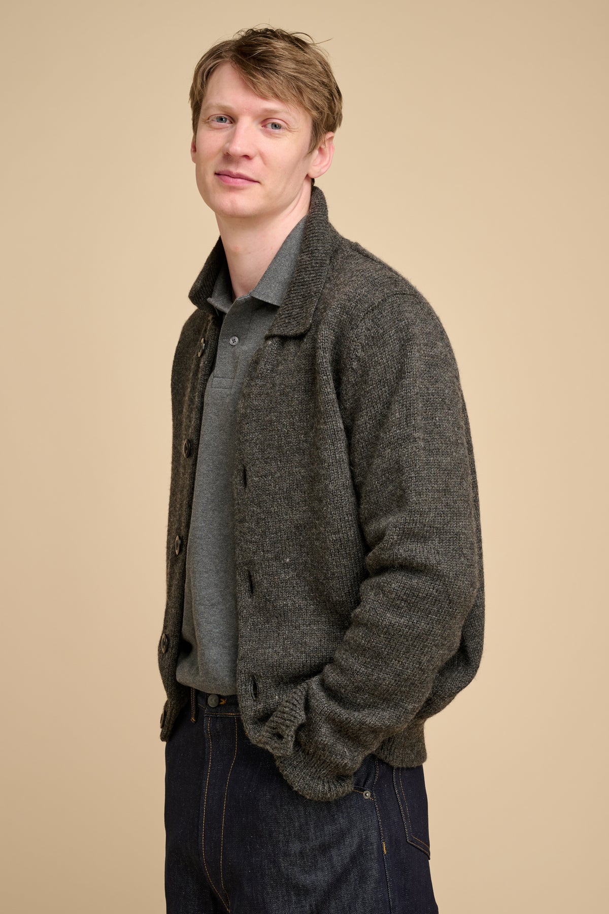 Man wearing grey cardigan against beige background.