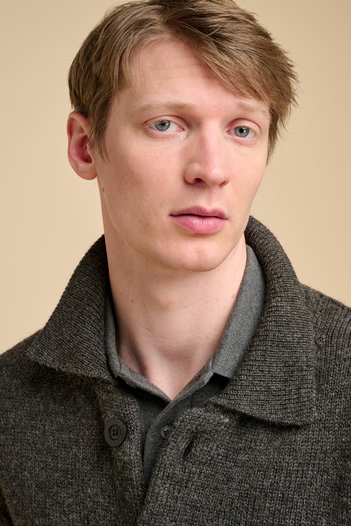 Man wearing grey cardigan against beige background.
