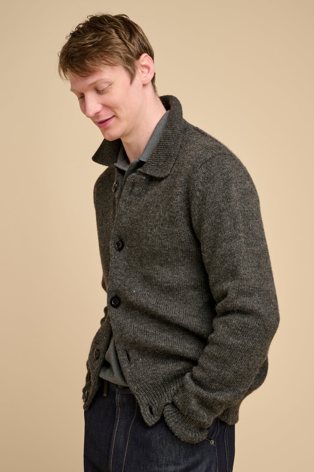 Man wearing grey cardigan against beige background.