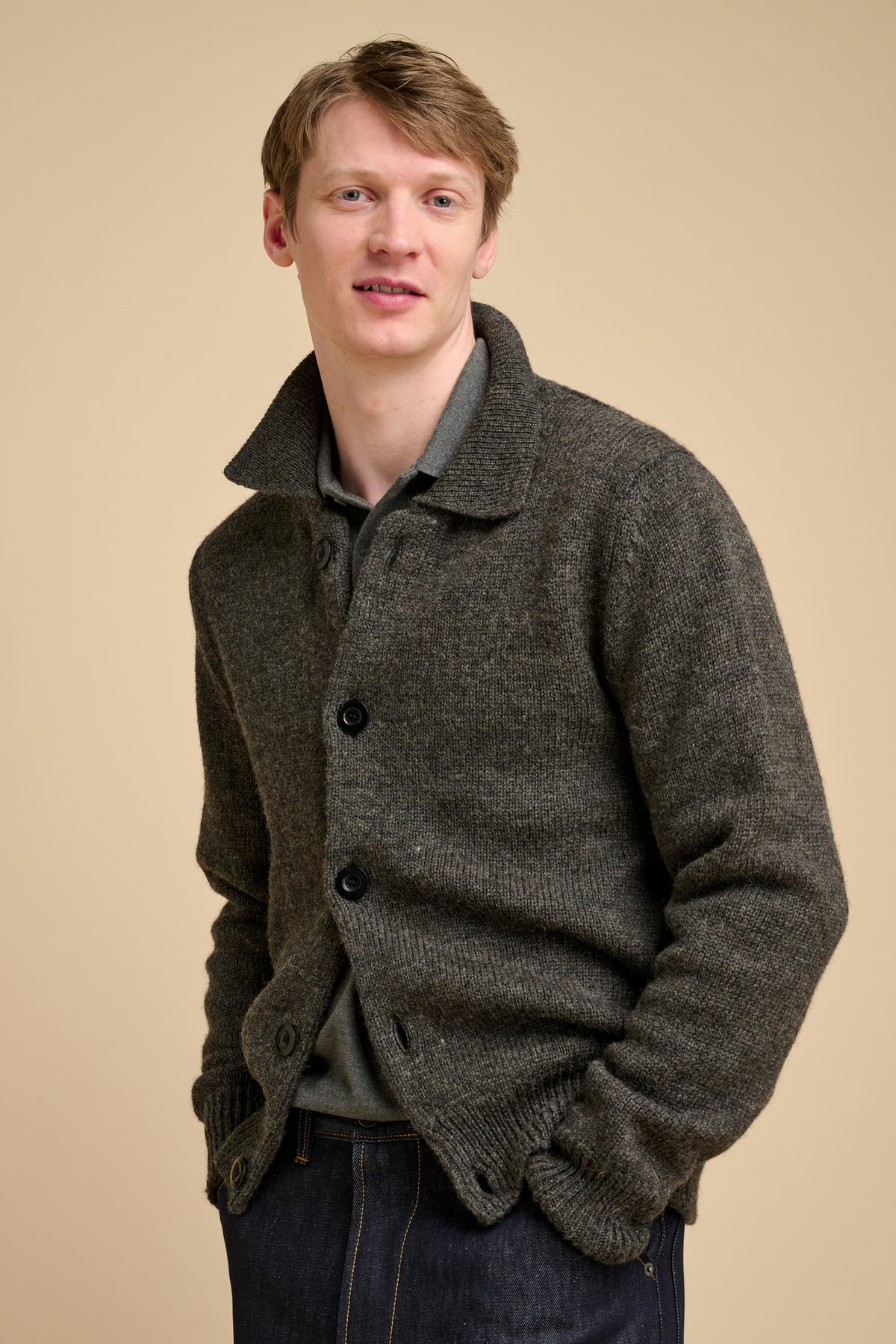 Man wearing grey cardigan against beige background.