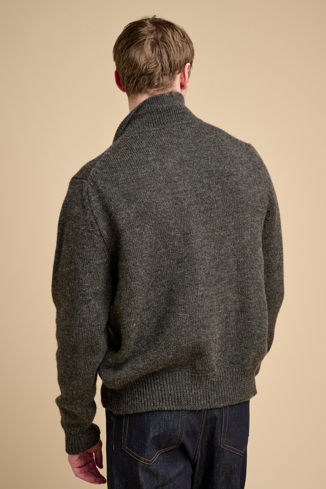 The back of man wearing grey cardigan against grey background.