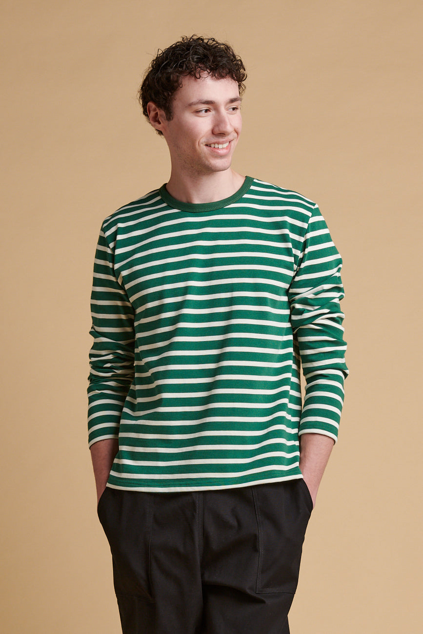Thigh up front of smiley male wearing bottle green ecru stripe long sleeve Breton top.
