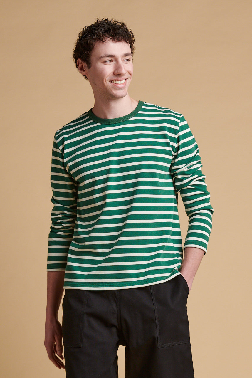 Thigh up front of smiley male wearing bottle green ecru stripe long sleeve Breton top.