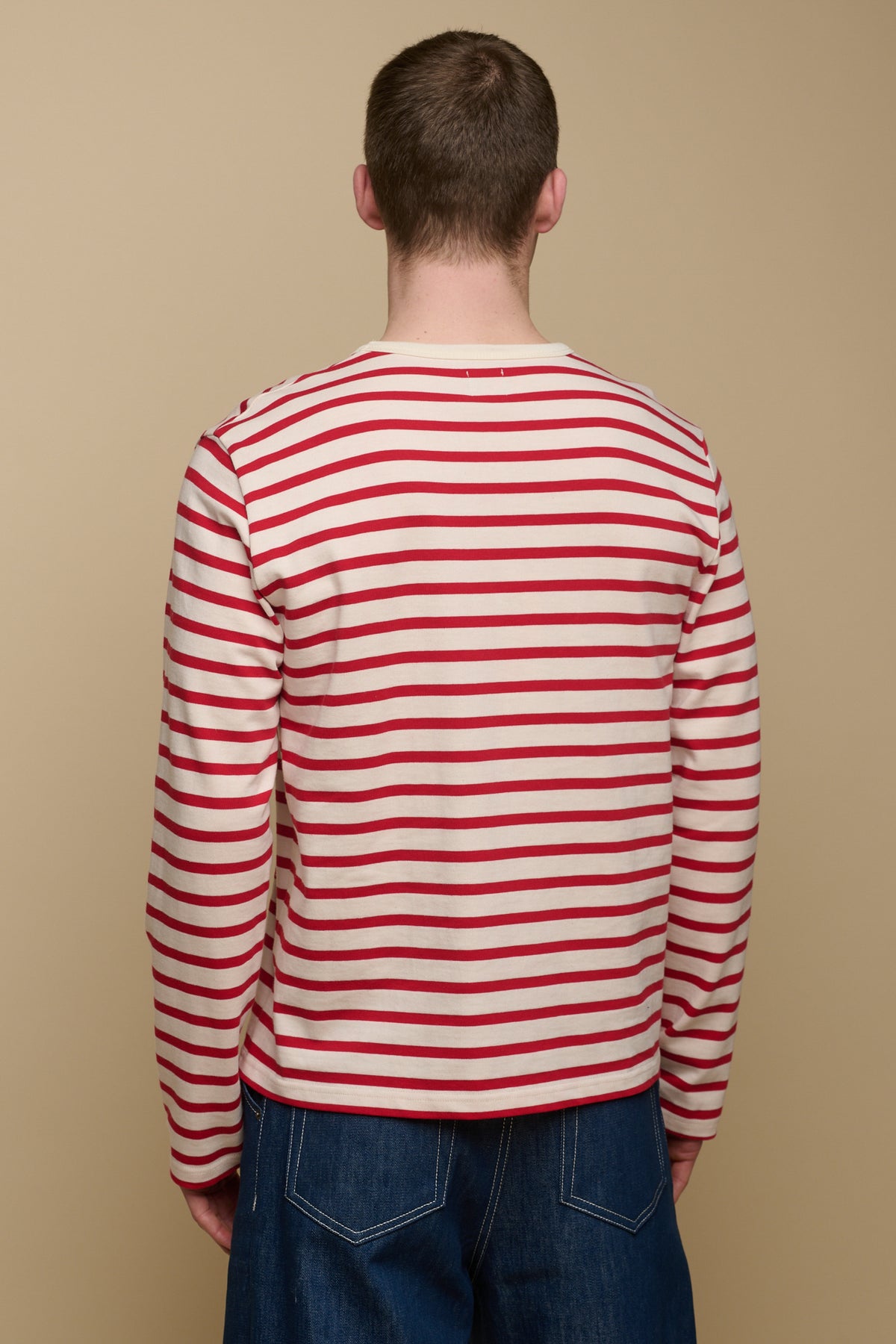 
            Thigh up of the back of brunet male wearing ecru/flame red Breton paired with men&#39;s jeans in blue