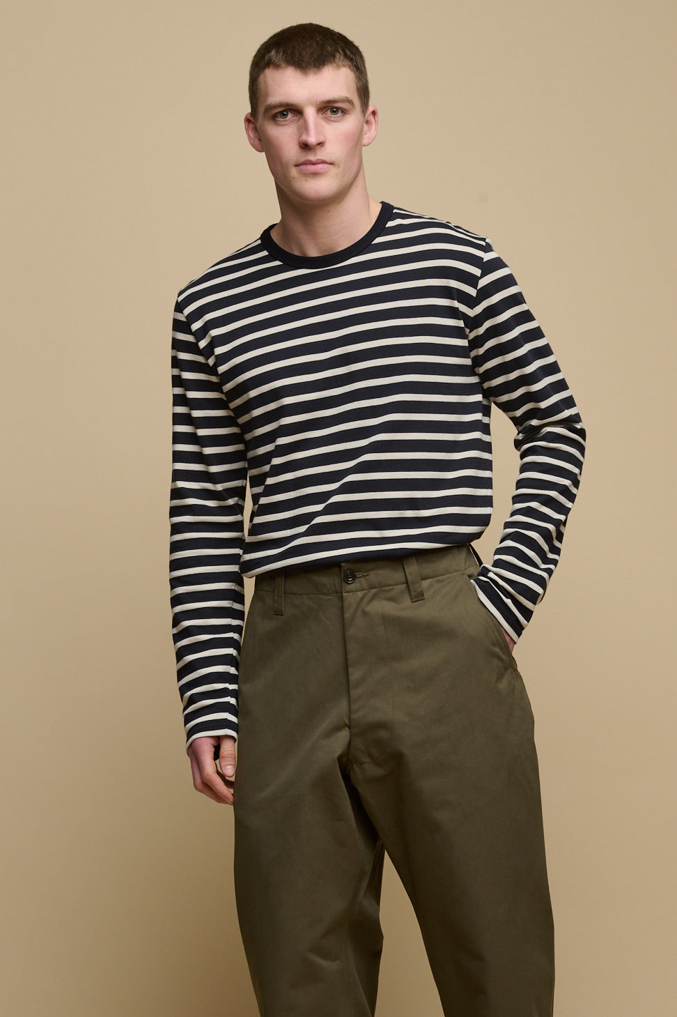 Thigh up image of male with shaved brunet hair wearing Breton in navy ecru tucked into olive field trousers