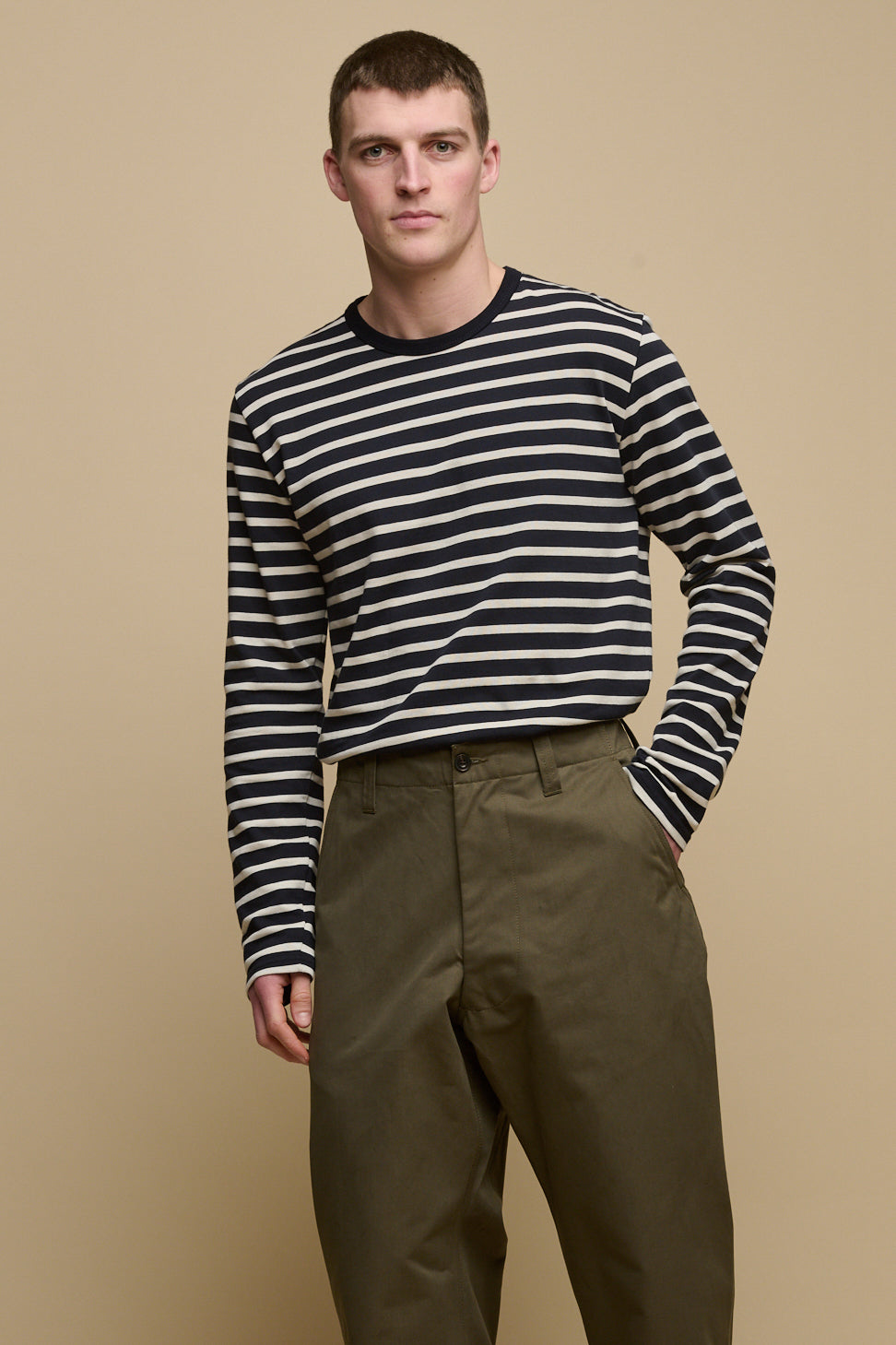 
            Thigh up image of male with shaved brunet hair wearing Breton in navy ecru tucked into olive field trousers