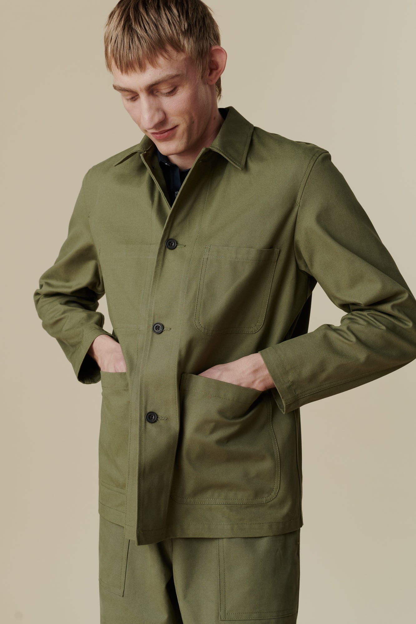 Image of white male wearing chore jacket in olive. Front pocket detail 