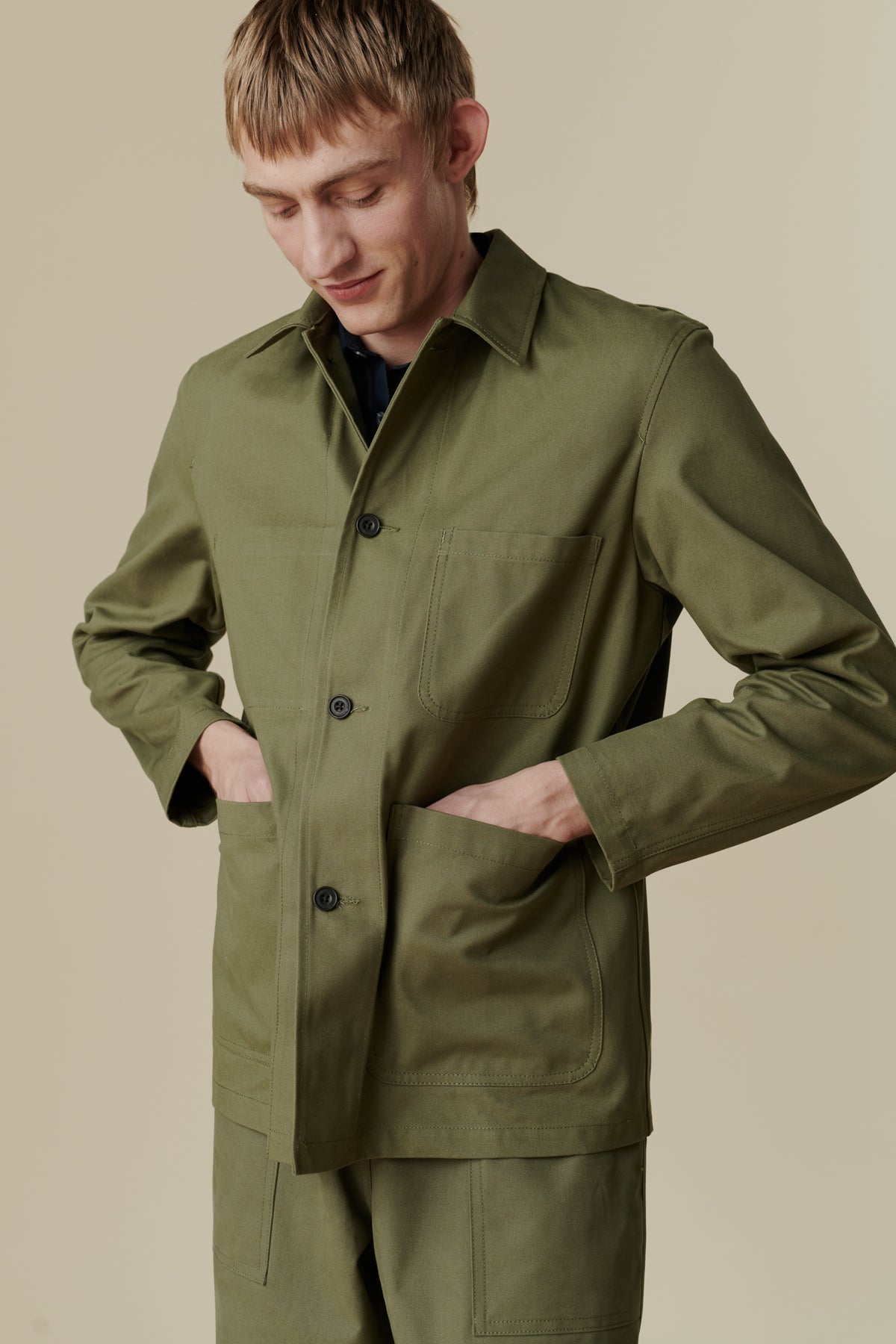
            Image of white male wearing chore jacket in olive. Front pocket detail 