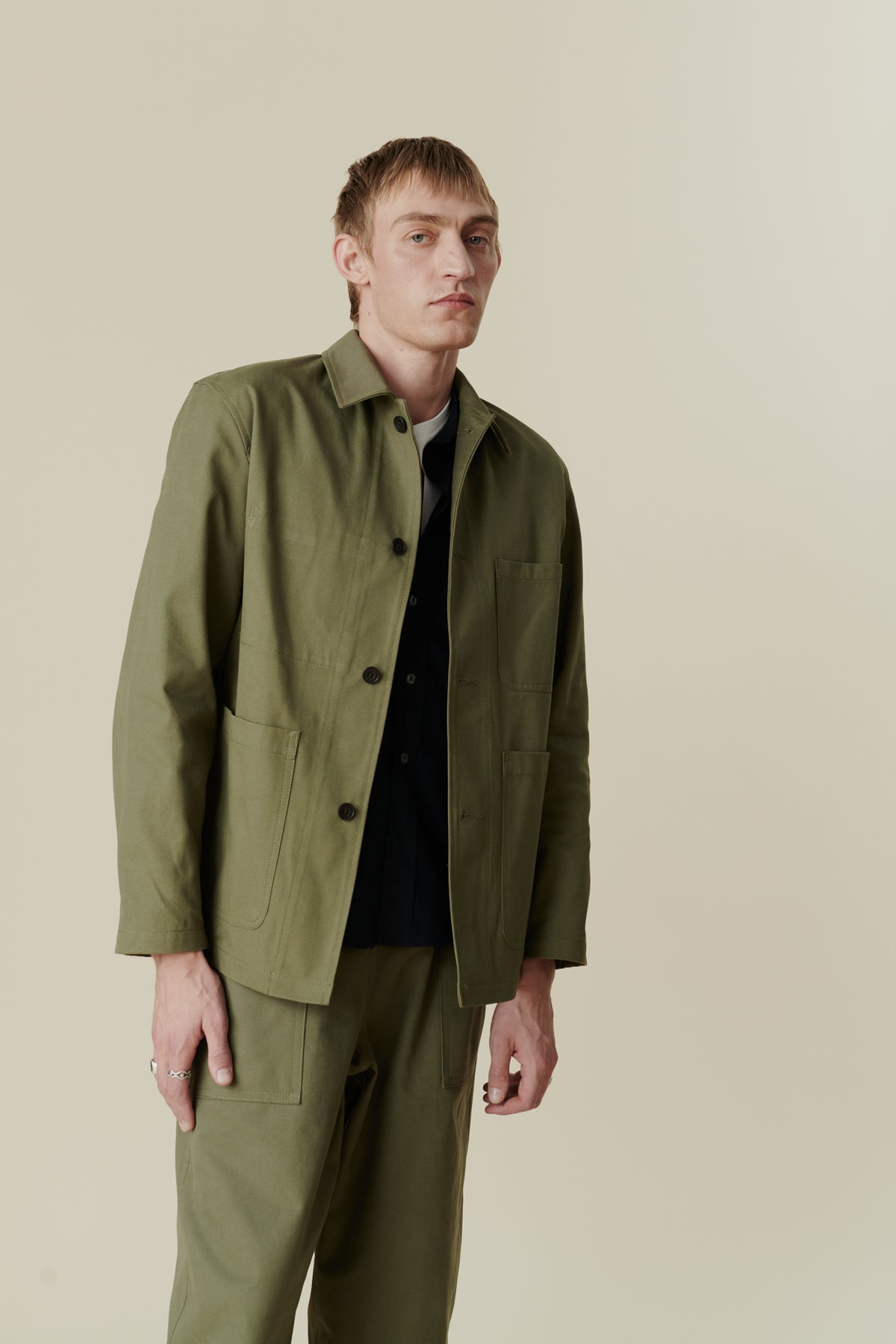 Image of white male, waist up wearing men's chore jacket in olive, worn with men's chore jeans in olive