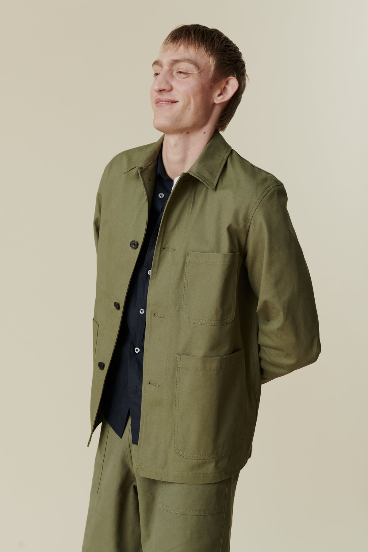 Image of white male, waist up wearing men's chore jacket in olive. Collar, button fastening detail, front pockets