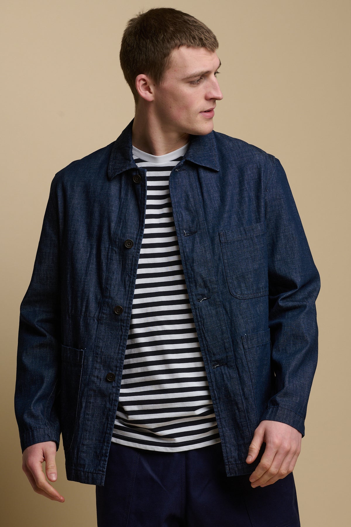 Thigh up image of male wearing open chore jacket in denim over striped t-shirt
