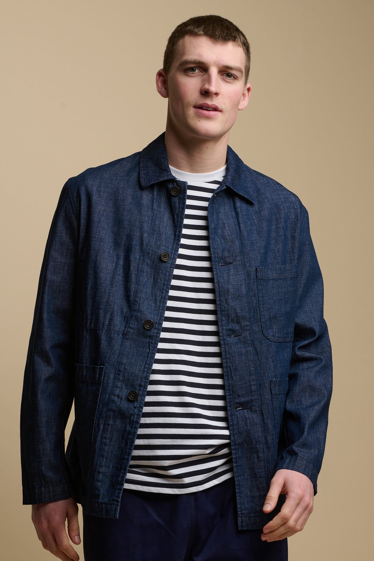 Thigh up image of male wearing chore jacket in denim over striped t-shirt.