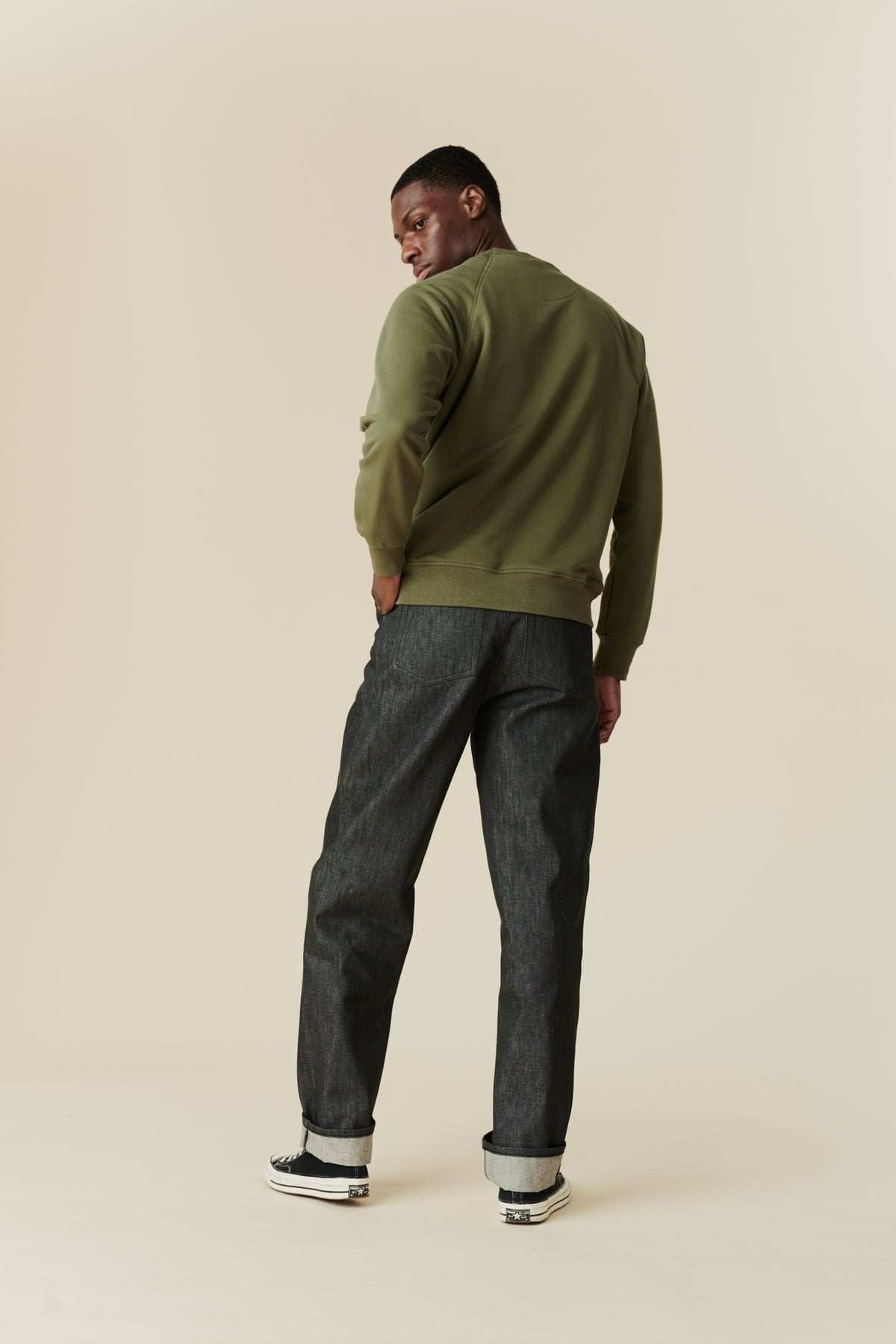 
            The back of black male wearing men&#39;s Chore jeans in black, wide leg and tapered fit with rolled hem, worn with olive green raglan sweatshirt