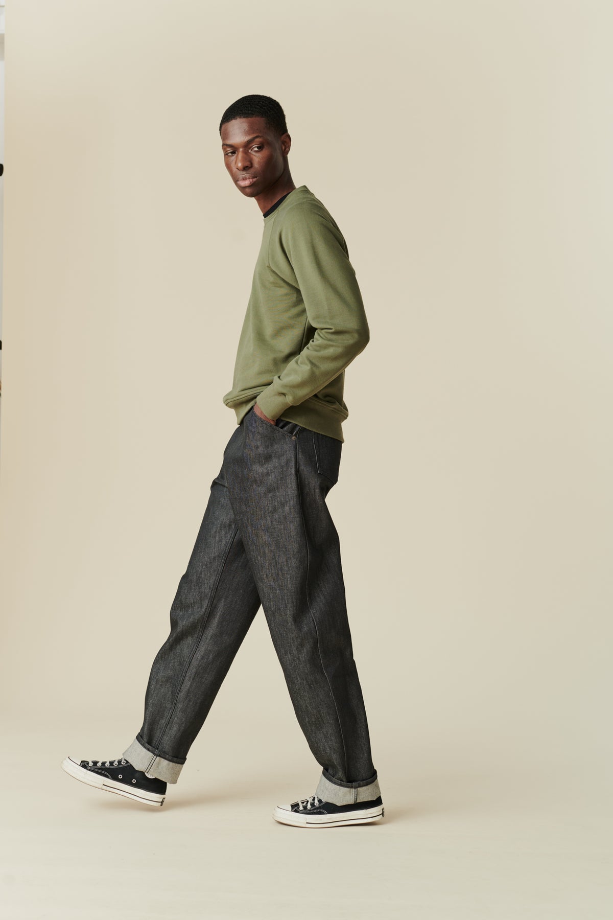 
            Side angle full body image of black male wearing men&#39;s Chore jeans in black, wide leg and tapered fit with rolled hem, worn with olive green raglan sweatshirt