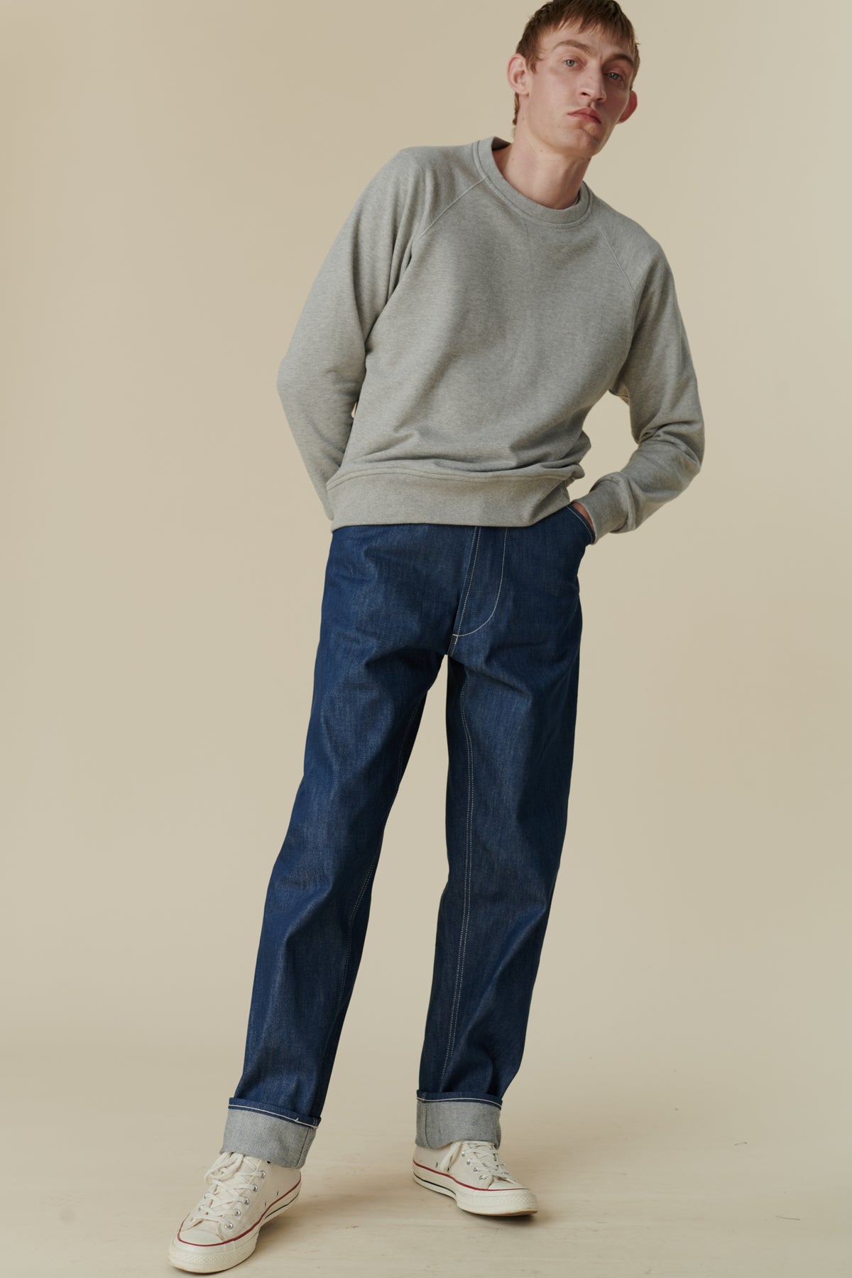 Full body image of white male wearing men's chore jean in blue paired with grey raglan sweatshirt