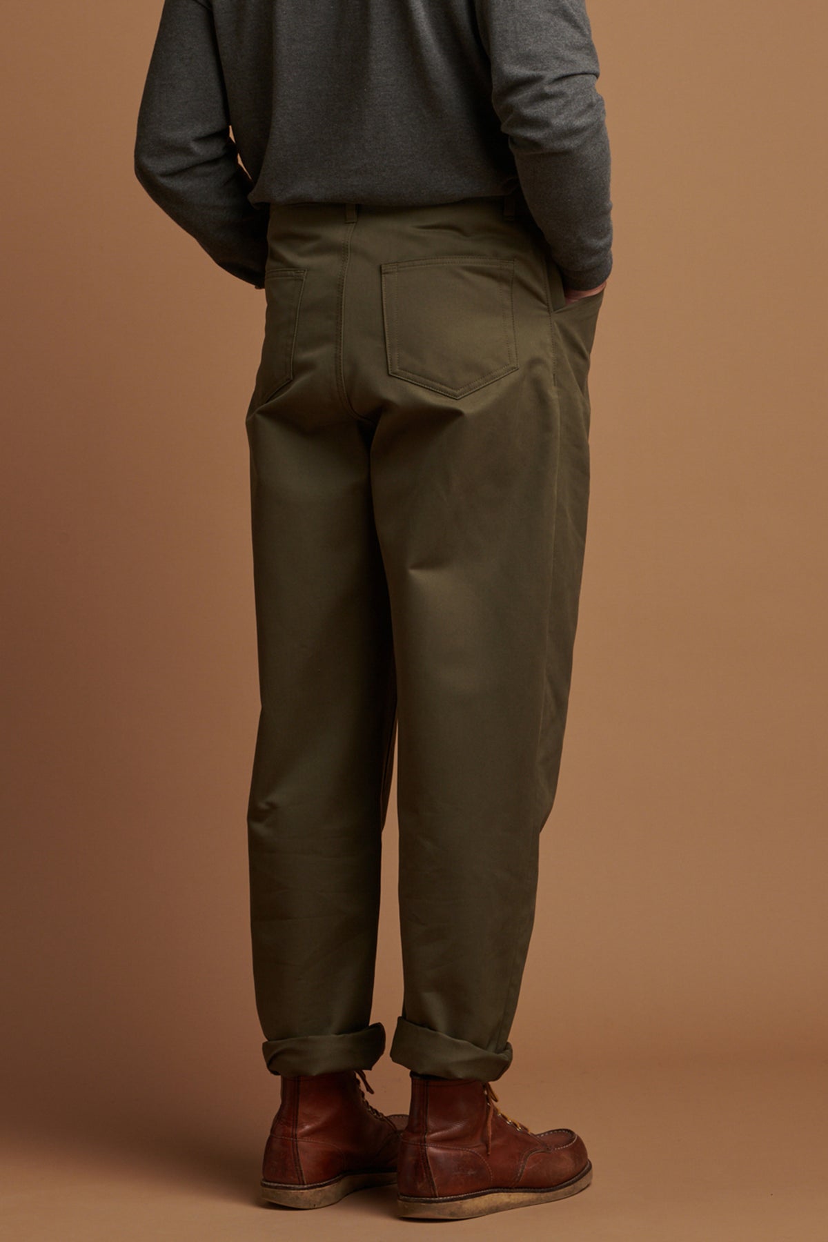 Person wearing olive green pants and brown shoes against a brown background