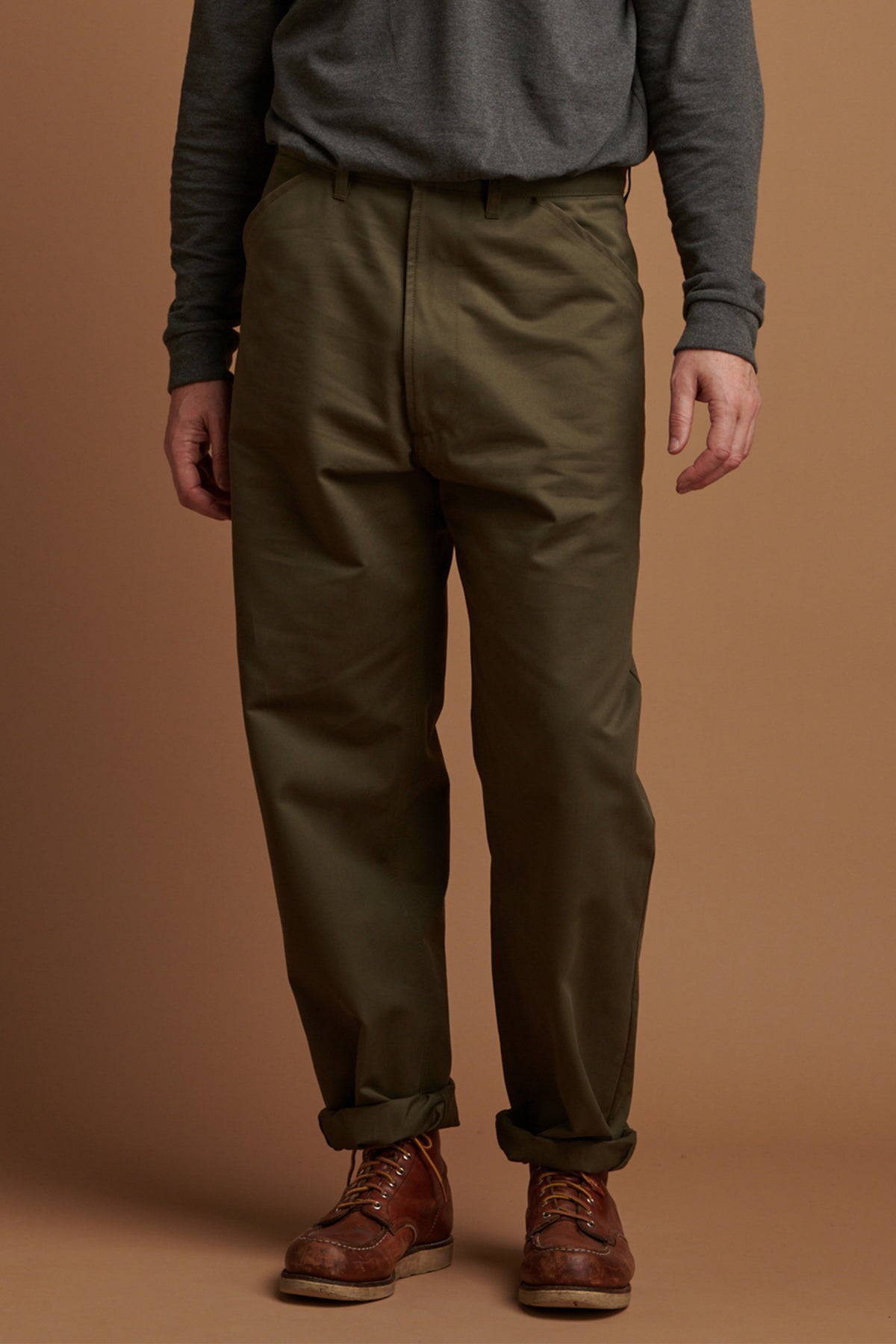 Person wearing olive green pants and brown boots on a brown background