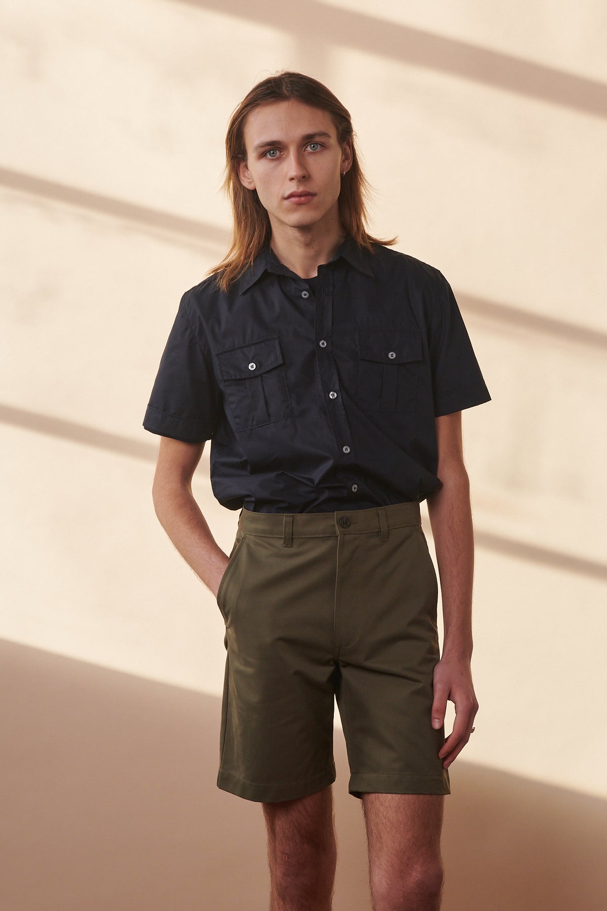 
            Male wearing classic shorts in olive with his hand in one of the front pockets paired with navy military shirt buttoned and tucked into shorts