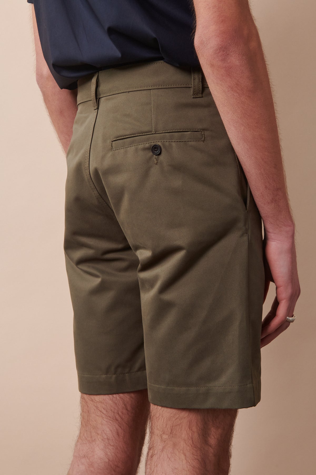 Details of the back of classic shorts in olive. One back pocket with button fastening and belt loops on the waistband.