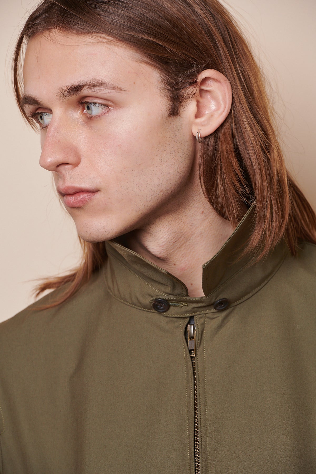 Portrait of male looking to the side wearing zipped collared Harrington jacket with collar turned up and button fastened underneath holding collar in place