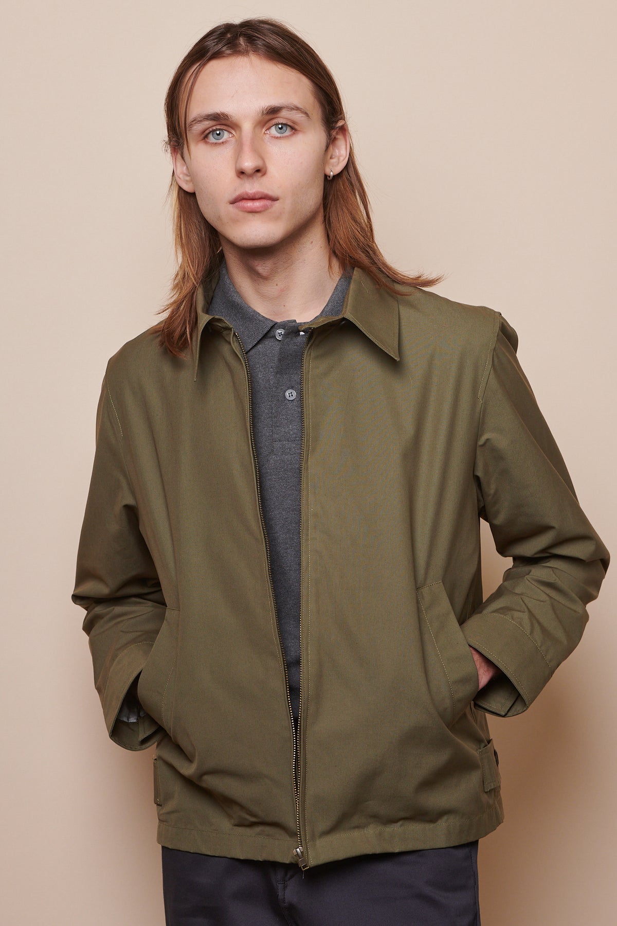 
            Thigh up image of male wearing unzipped collared Harrington jacket in olive with both hands in front pockets 