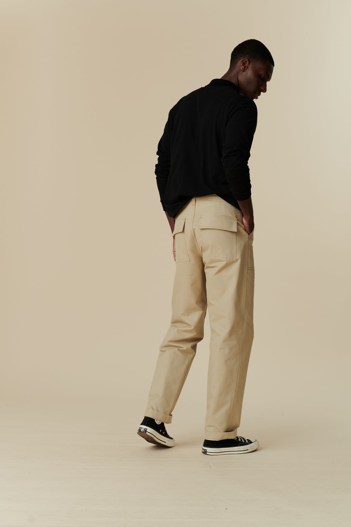 Full body image of back of black male wearing combat trouser in putty, worn with long sleeve polo shirt in black