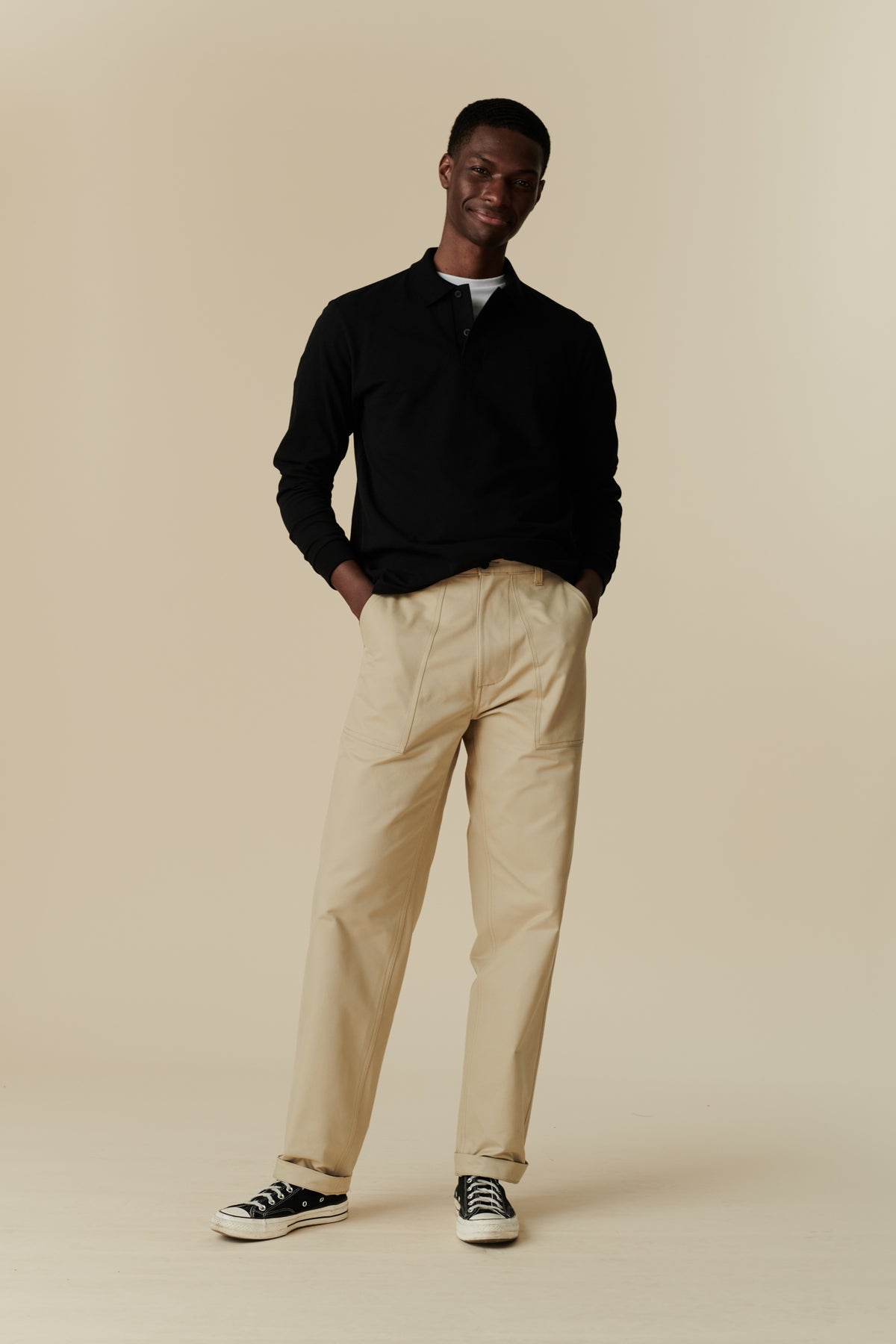 Full body image of black male wearing combat trouser in putty, worn with long sleeve polo shirt in black