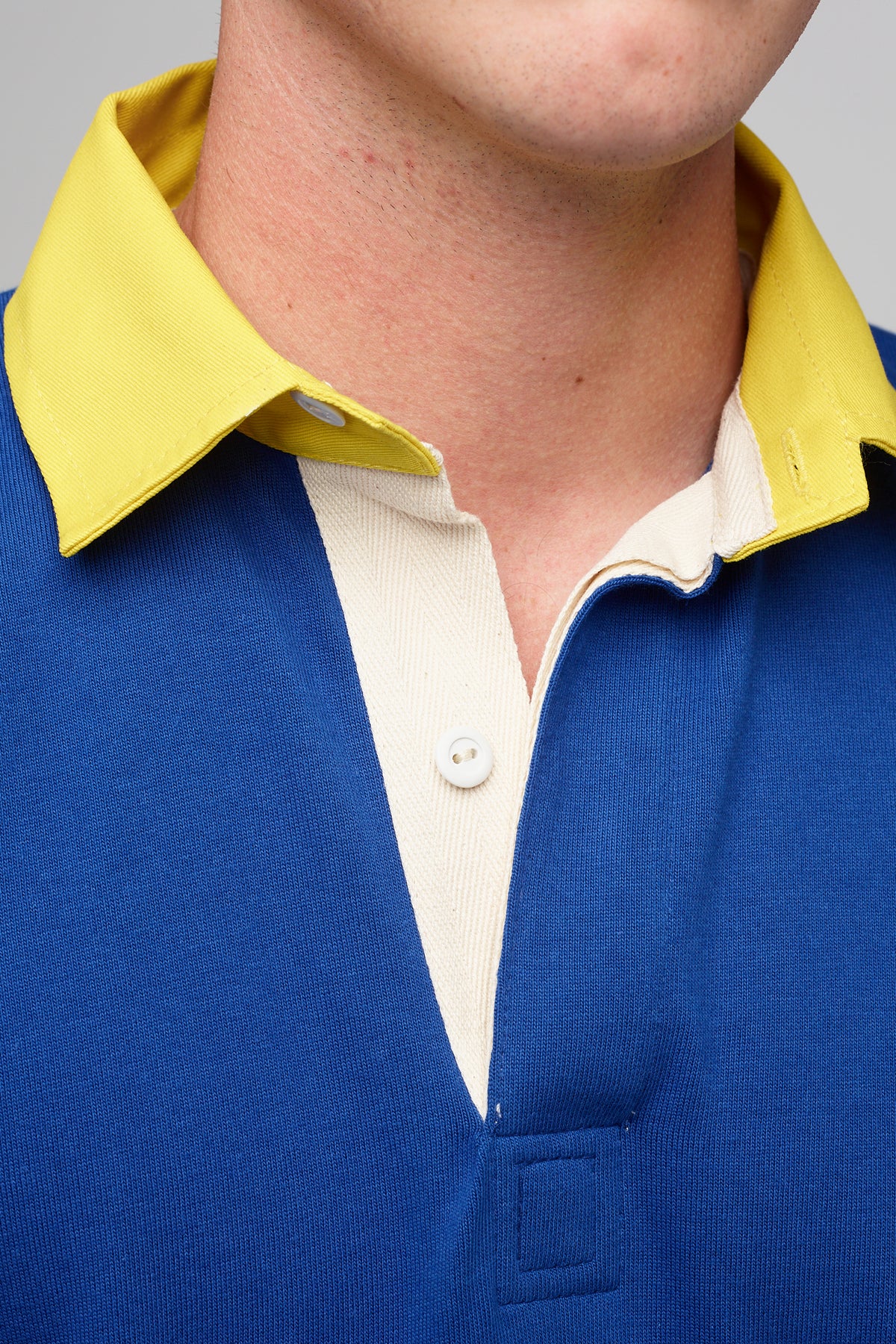 
            White, male wearing blue rugby shirt, contrast yellow unbuttoned collar, cream placket