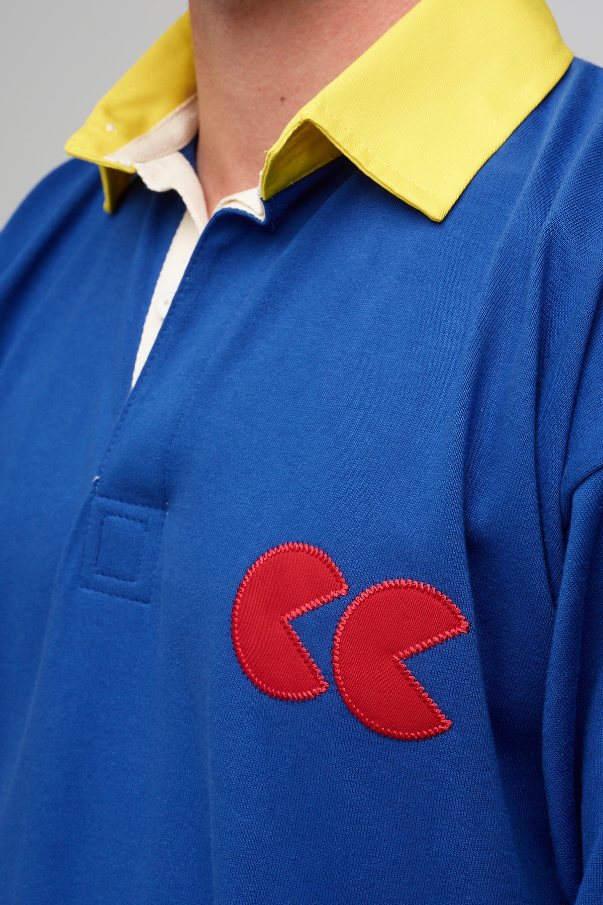 
            White,  male wearing blue rugby shirt, contrast yellow collar, red CC logo badge applique detail