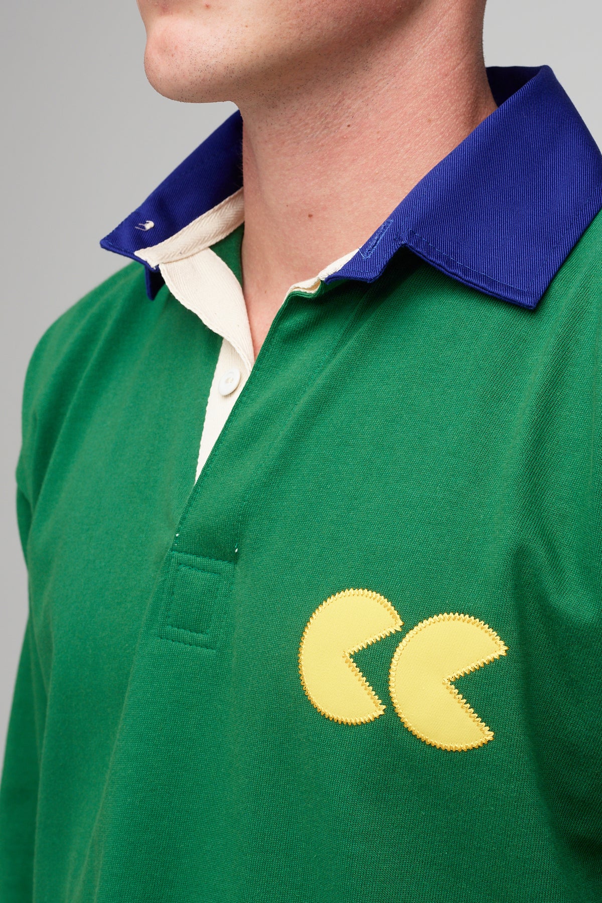 White, male, wearing green rugby shirt with contrast blue collar, yellow CC logo badge applique detail