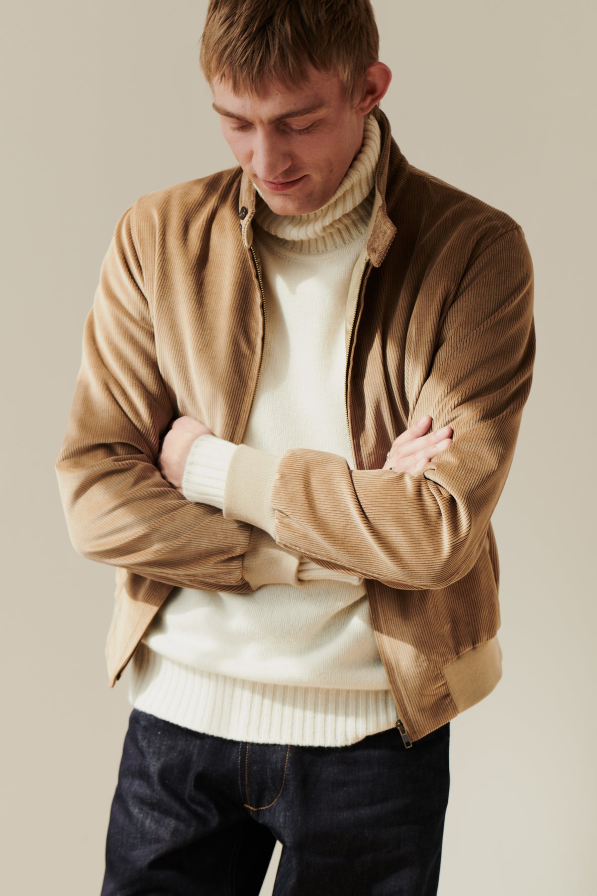 
            Blonde, white male wearing men&#39;s corduroy harrington jacket in stone layered over lambswool roll neck jumper in ecru