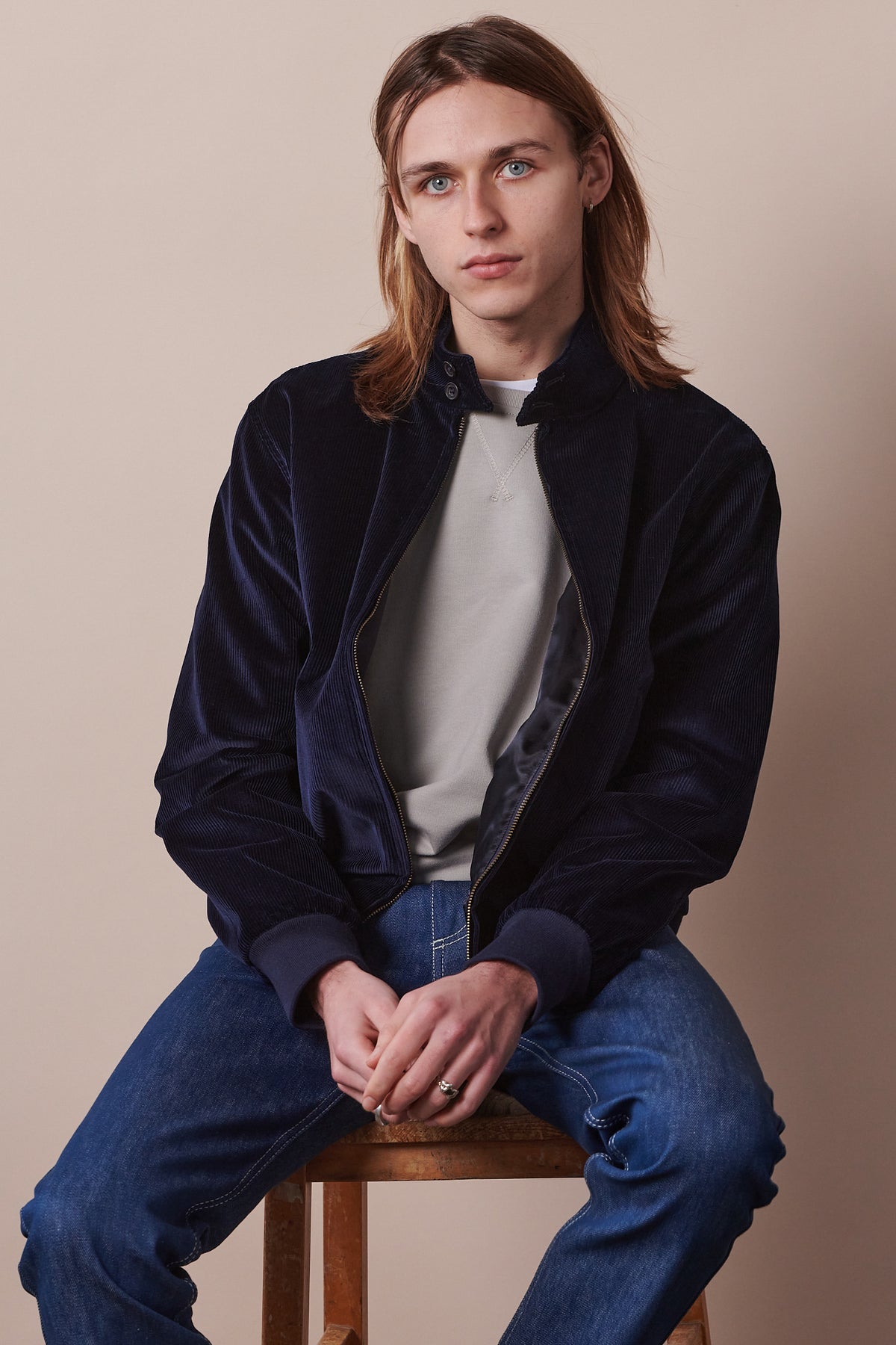 
            Image of male sat on stool wearing navy corduroy Harrington paired with blue jeans