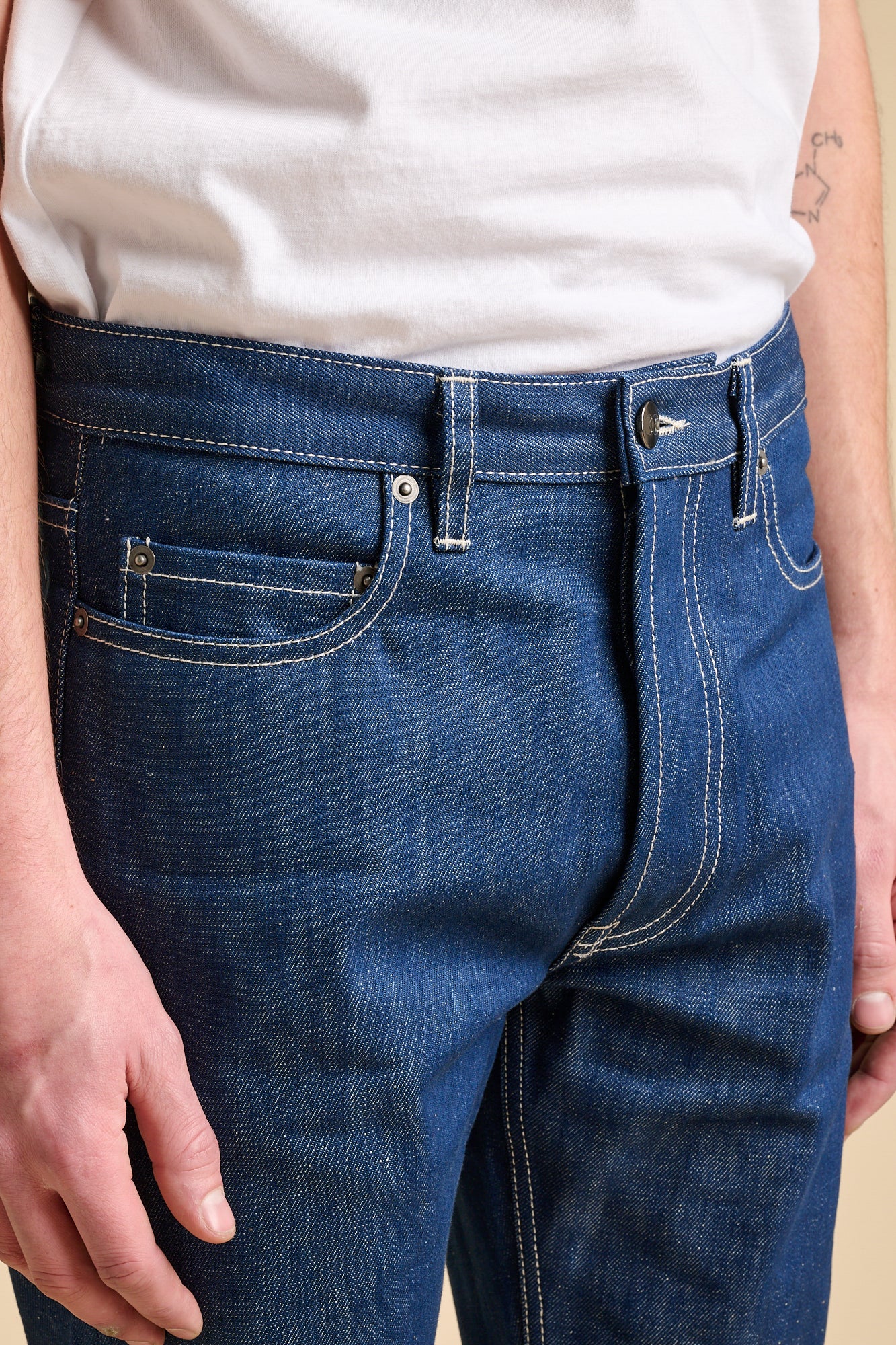 Close up of the man wearing blue jeans with contrast ecru stitching. Front pockets, and coin pocket.
