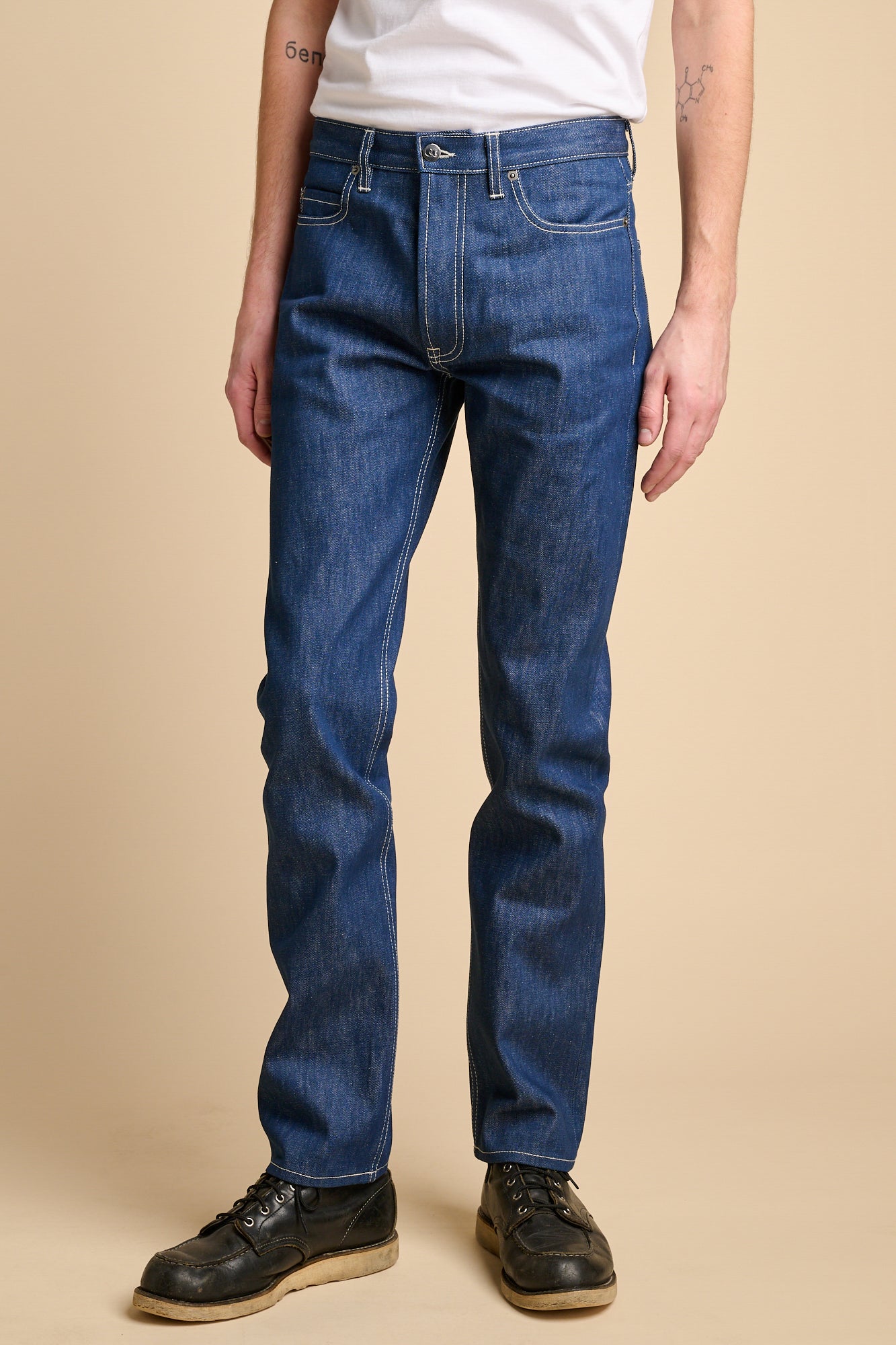 Man wearing straight cut jeans in blue with contrast ecru stitching.