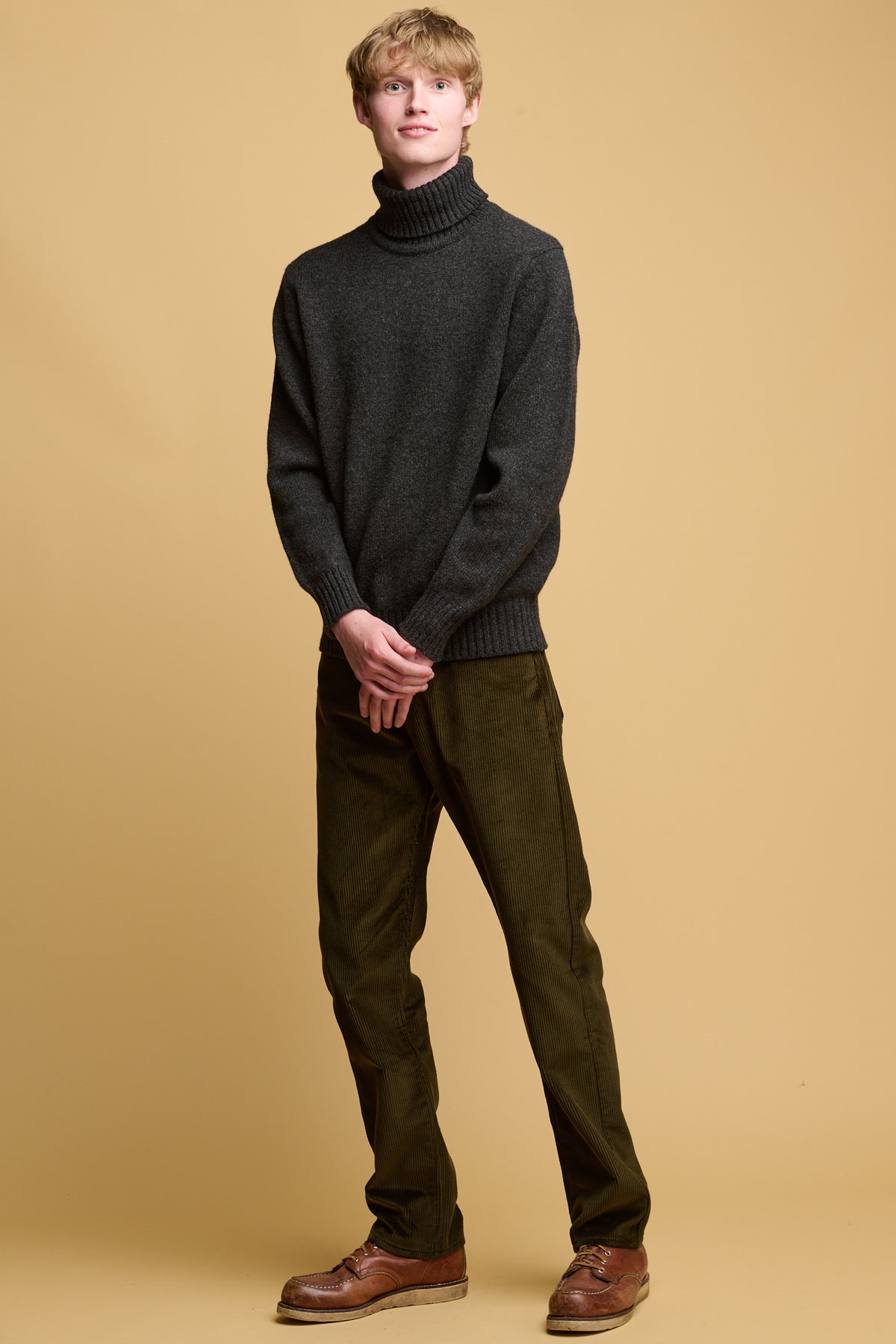 Male wearing five pocket cord trousers in dark olive paired with lambswool roll neck jumper in charcoal