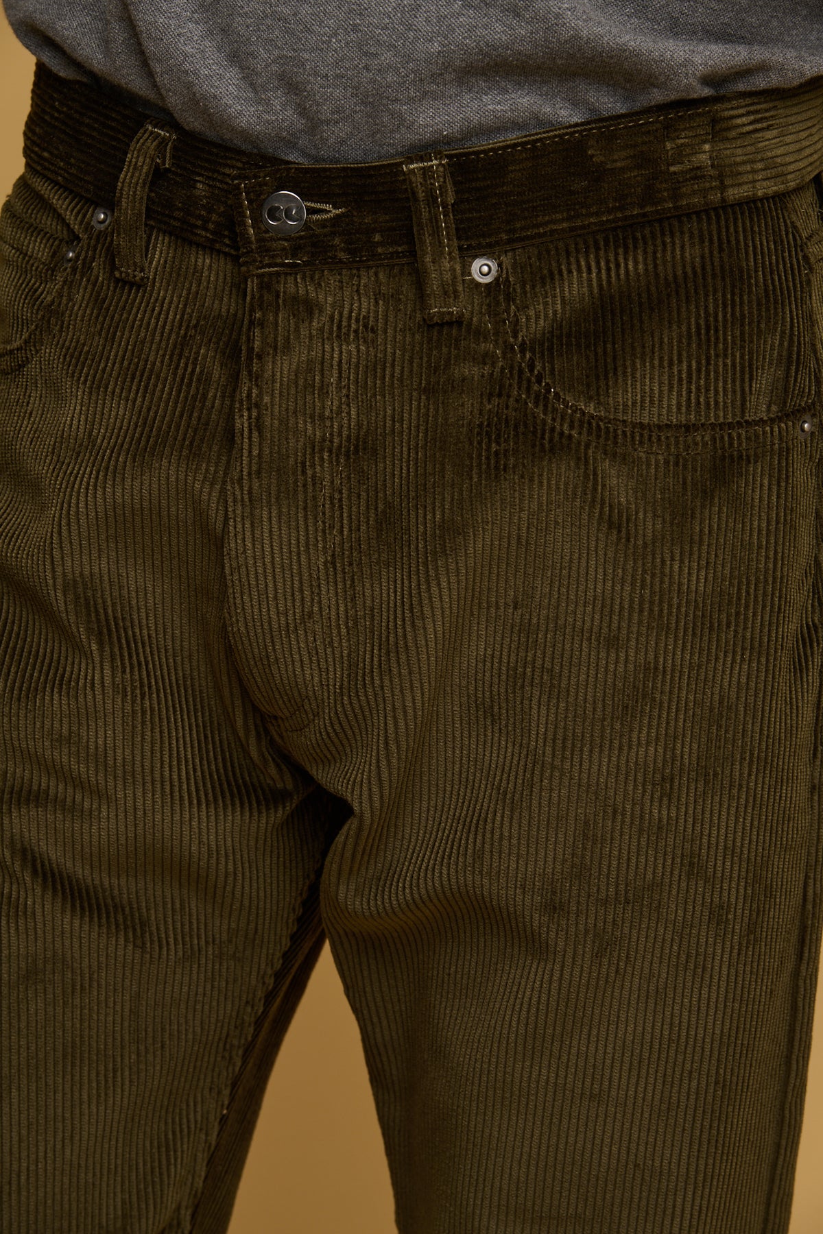 Close up of the front of the waistband, pockets and fly of cord trousers in olive. CC logo silver button fastening