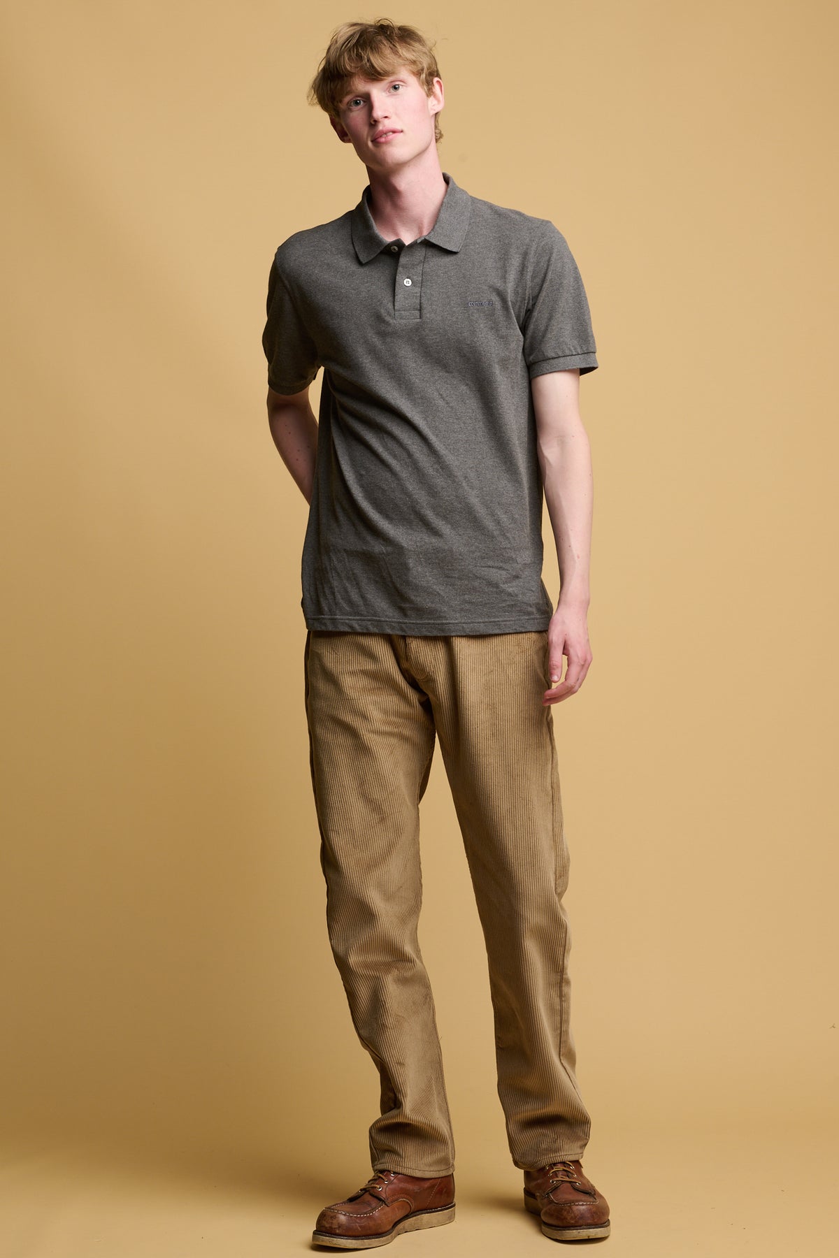 white male wearing five pocket cord trousers in stone paired with short sleeve community clothing polo shirt in grey