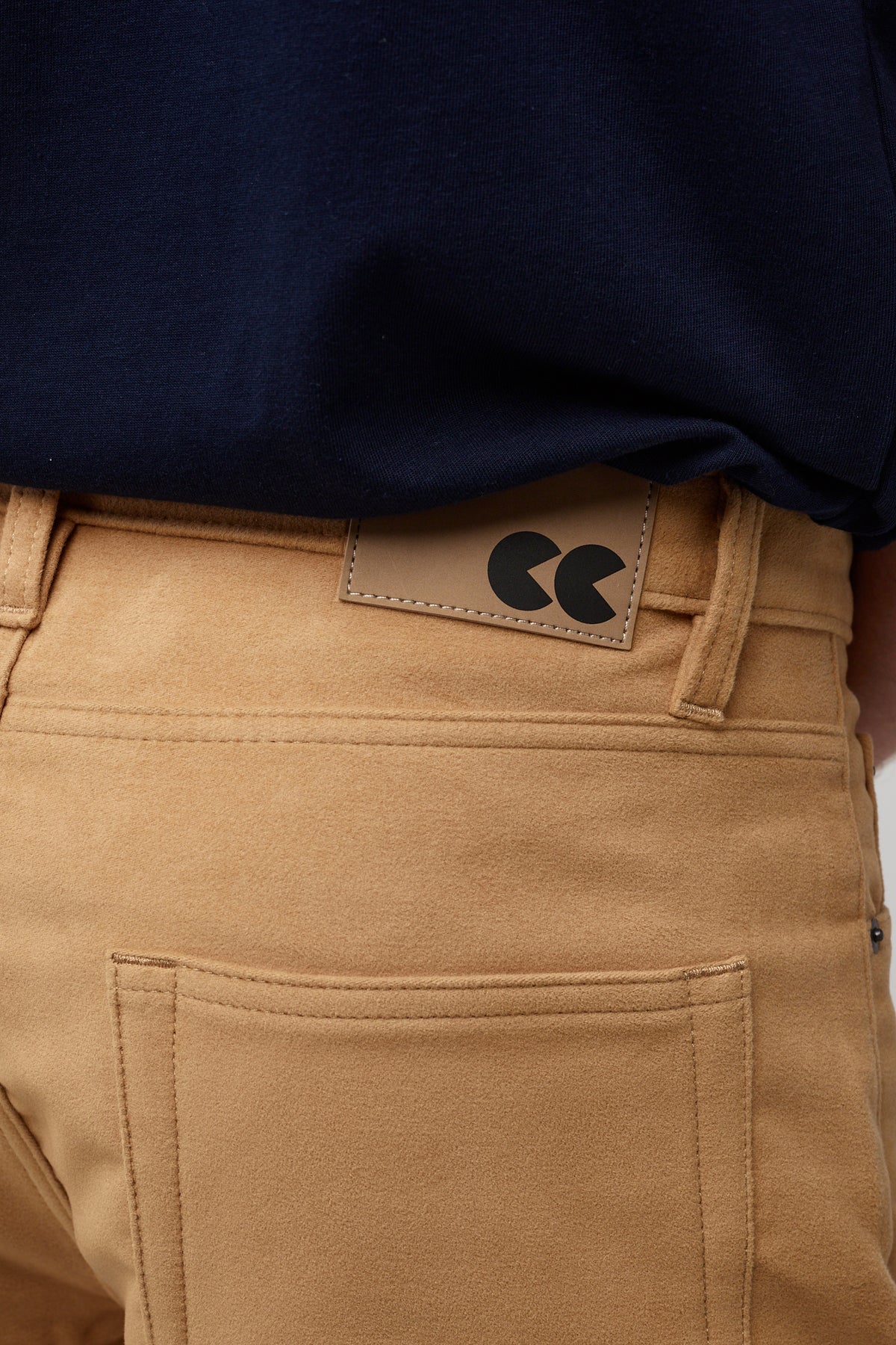 Male brunette wearing five pocket moleskin jeans in camel styled with black t-shirt, pocket and CC logo badge close up
