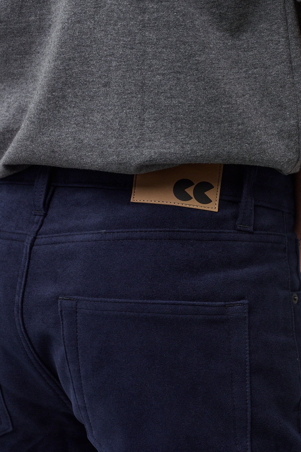 Brunette male in navy Five Pocket Moleskin Jean styled with charcoal short sleeve t-shirt, back pocket and brown CC jean badge close up