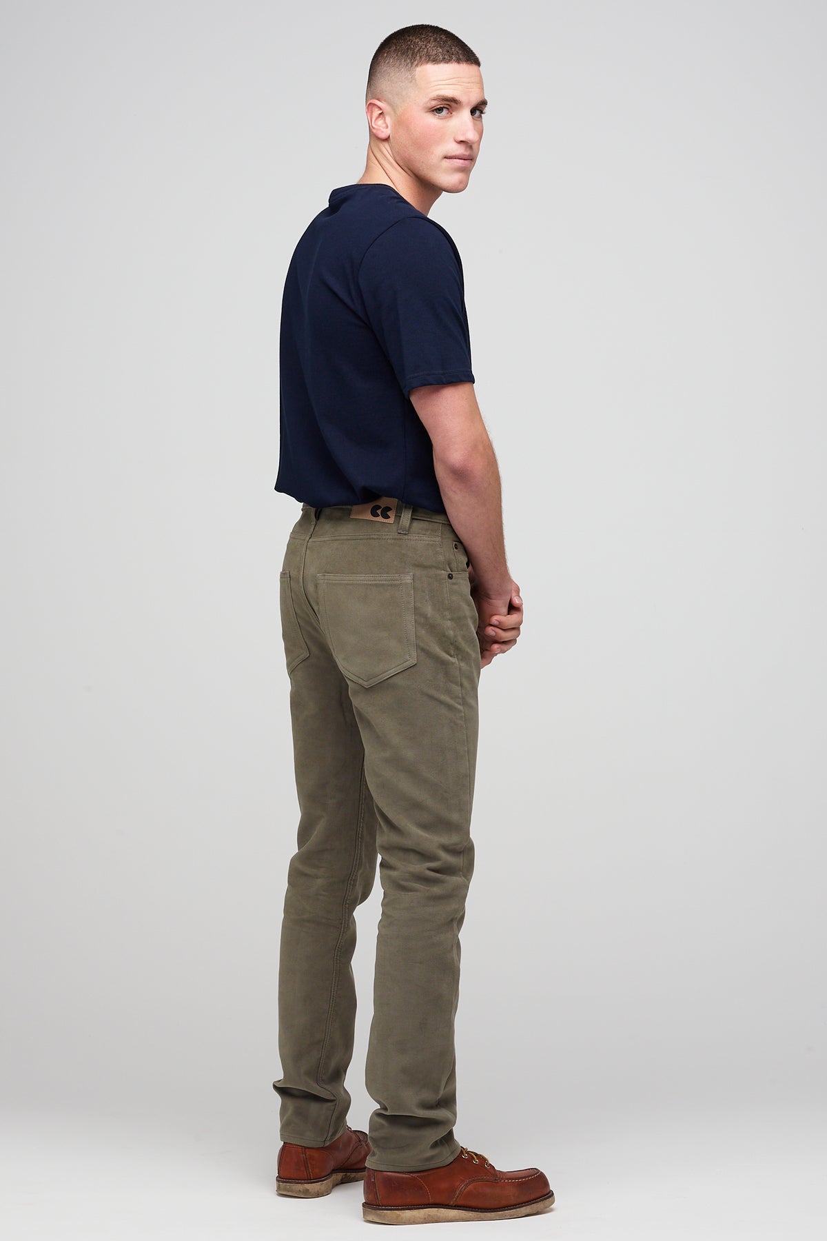 
            Brunette male in Olive Five Pocket Moleskin Jean styled with navy men&#39;s short sleeve t-shirt back pocket