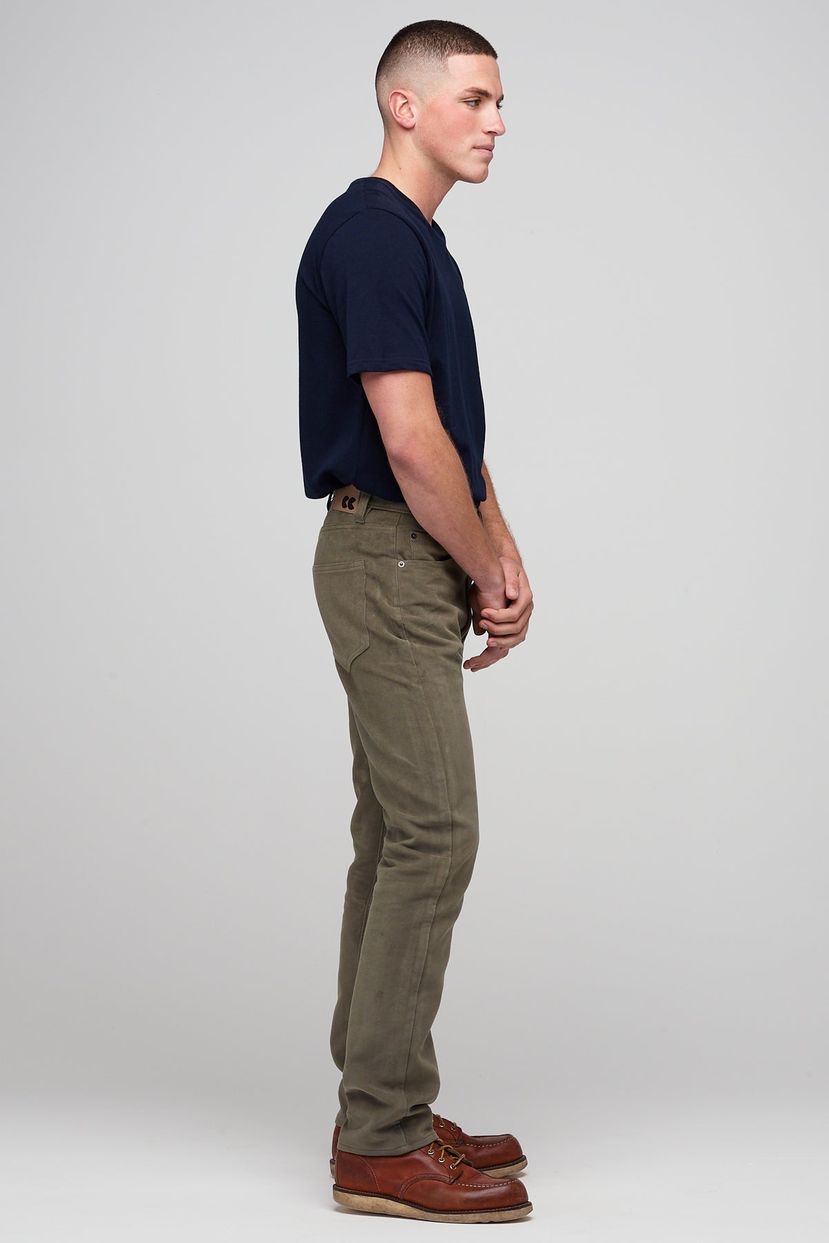 
            Brunette male in Olive Five Pocket Moleskin Jean styled with navy men&#39;s short sleeve t-shirt