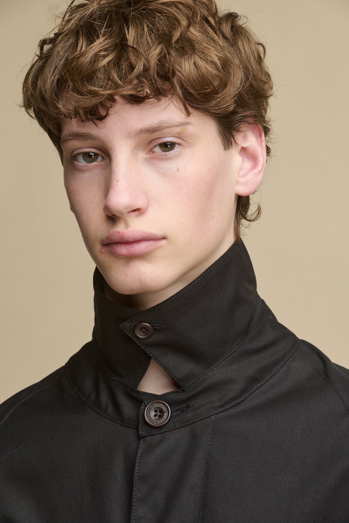 Portrait of white male wearing Frank Raglan Belted Raincoat withcollar butooned up with Community Clothing logo brown buttons