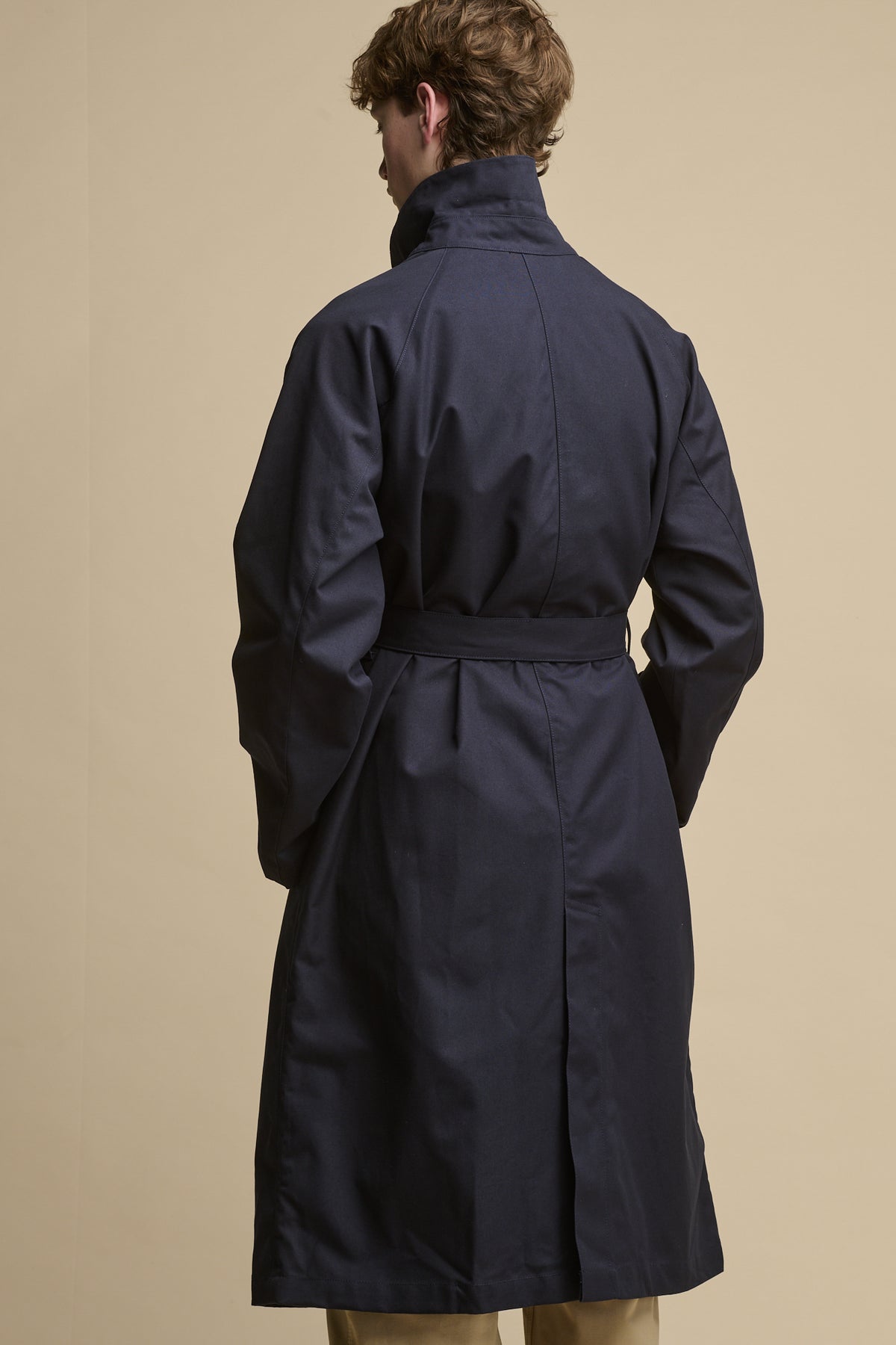 the back of male wearing Frank Raglan Belted Raincoat with belt fastened and collar up.