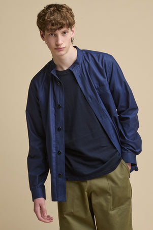 Thigh up image of male wearing George Lightweight Collarless Overshirt unbuttoned over navy t shirt paired with Cameraman Pants in olive