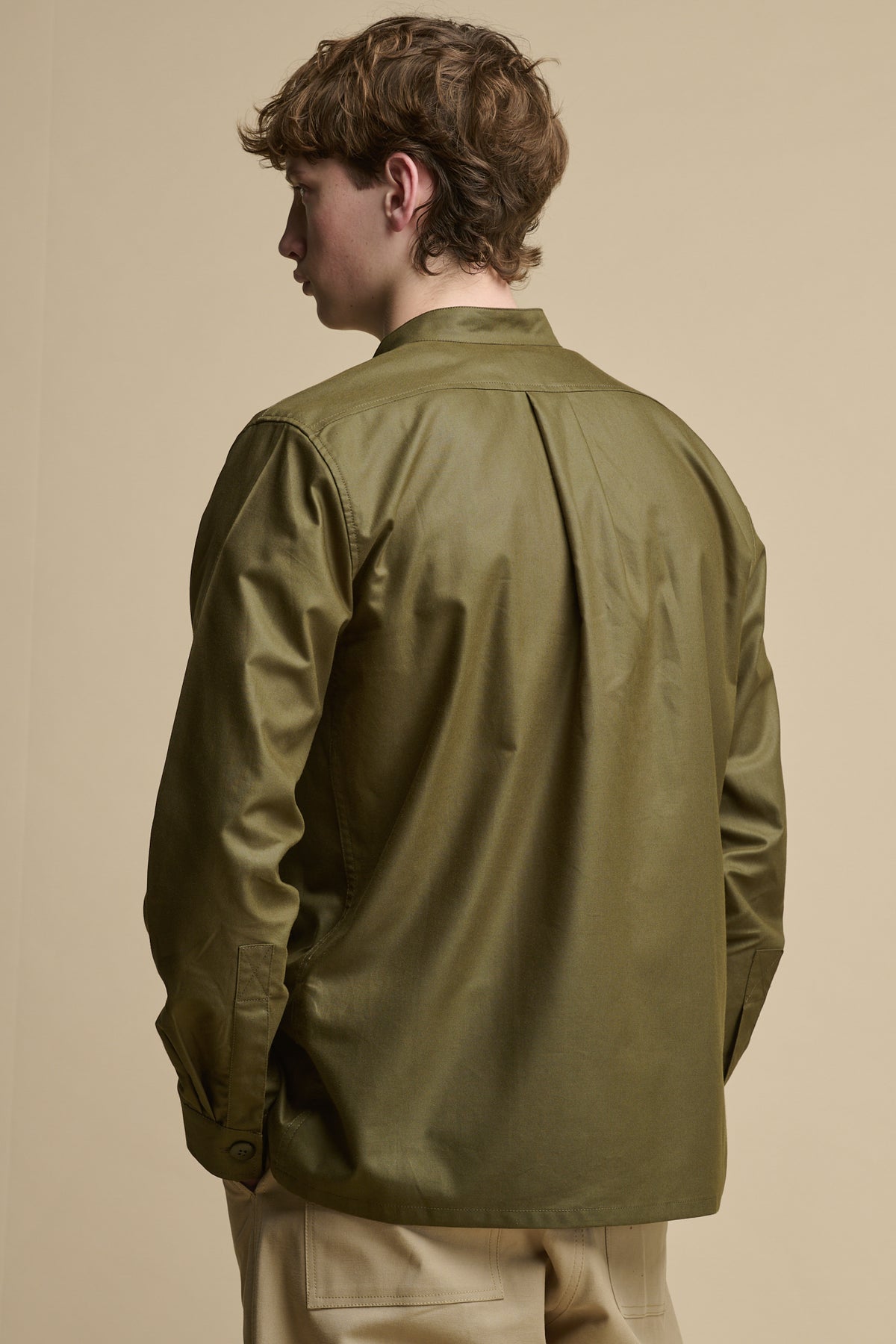 
            The back of men&#39;s George Lightweight Collarless Overshirt in Olive with back pleats and button fastening on cuff